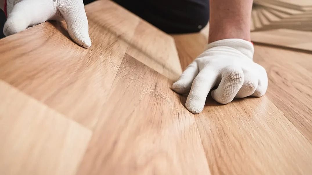 A person wearing white gloves is installing a wooden floor.