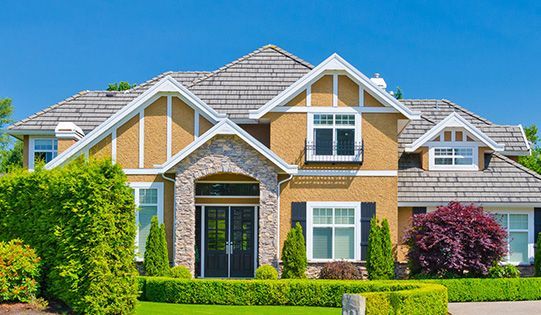 A large house with a lush green lawn and a blue sky in the background.