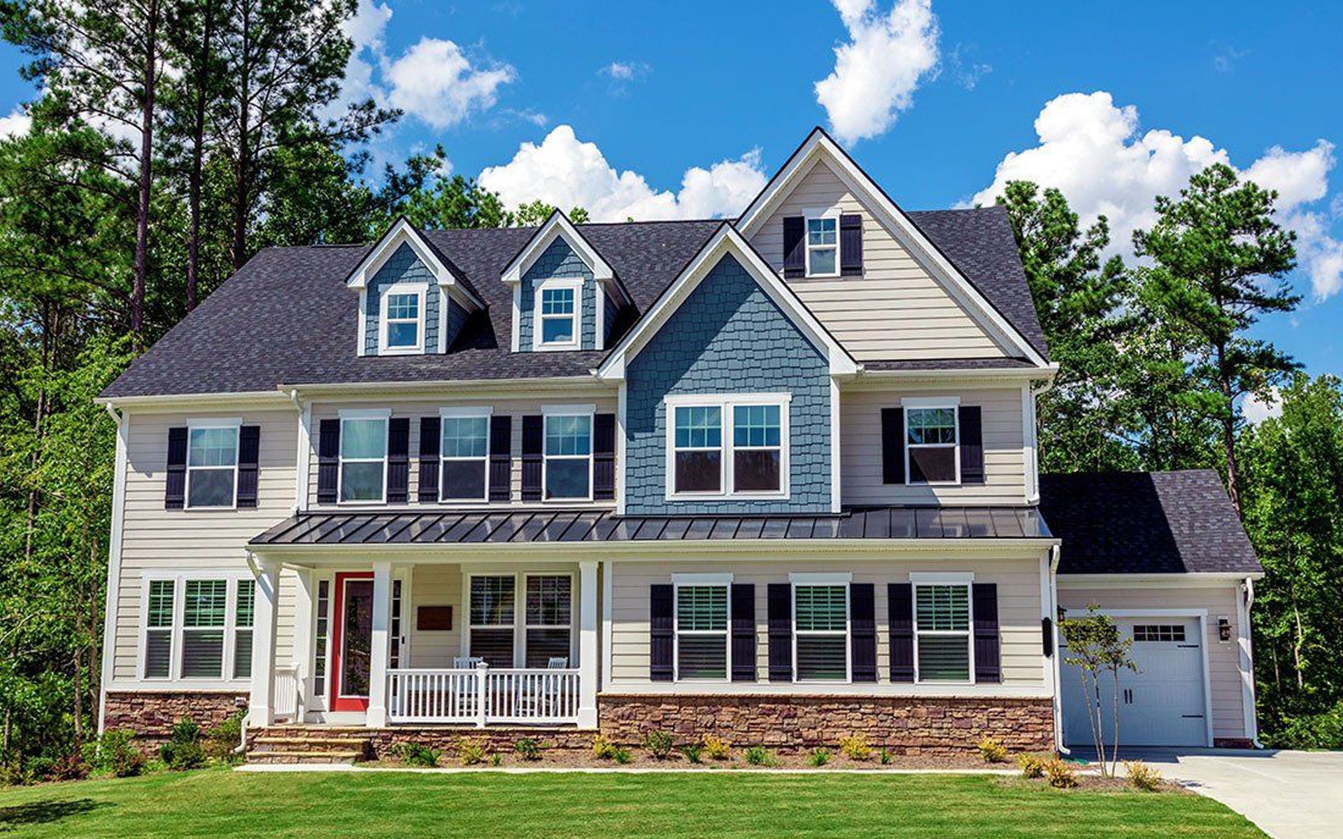 A large house with a blue siding and black shutters is sitting on top of a lush green lawn.