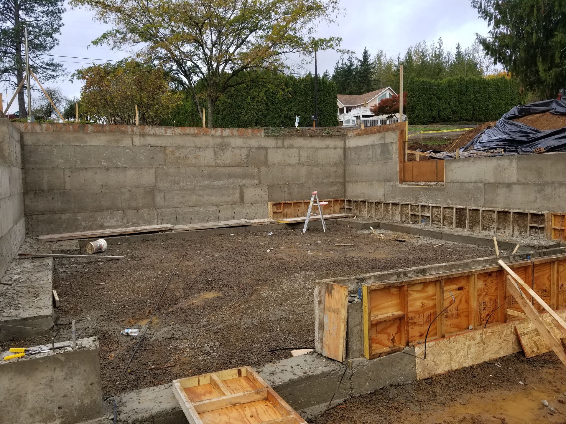 Partially built concrete foundation with retaining walls and wooden forms in a backyard construction site