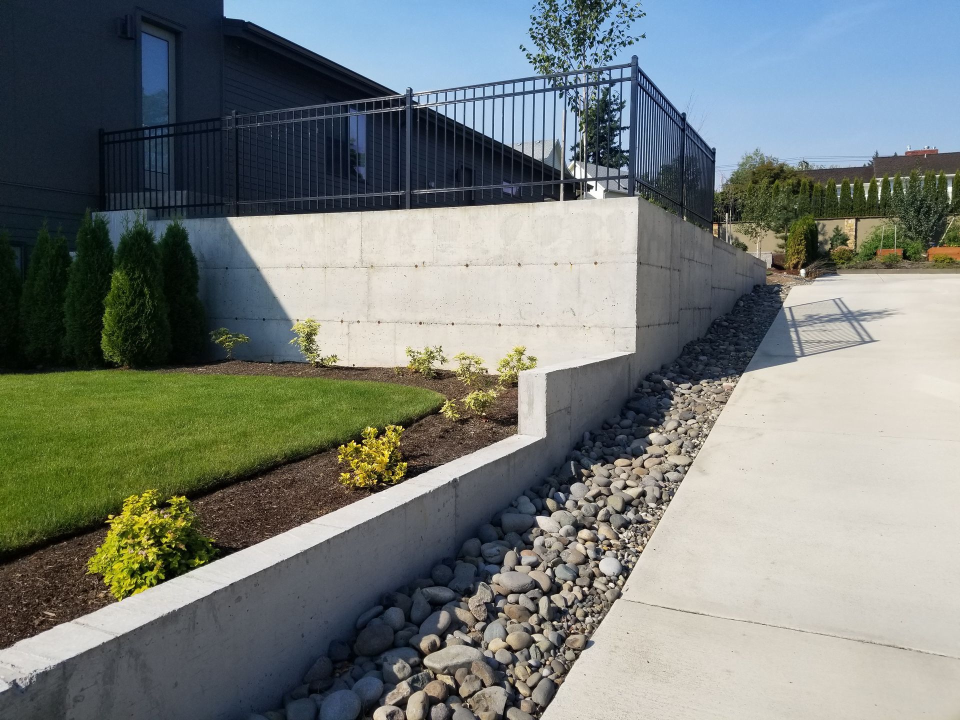 Modern building exterior with ramp, concrete retaining wall, and landscaped rocks along a sidewalk