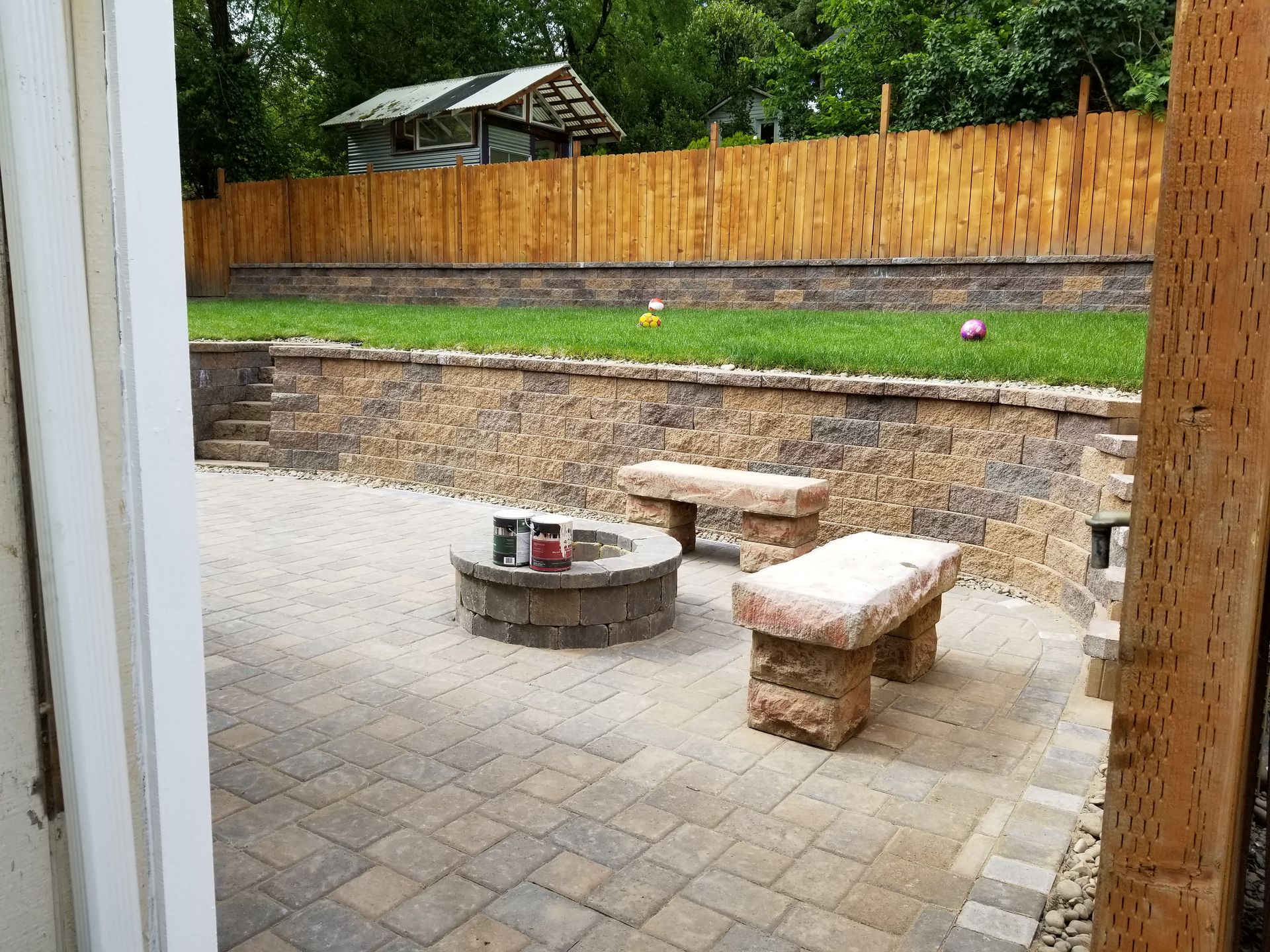 Patio with stone fire pit and benches in a fenced backyard, viewed from a doorway