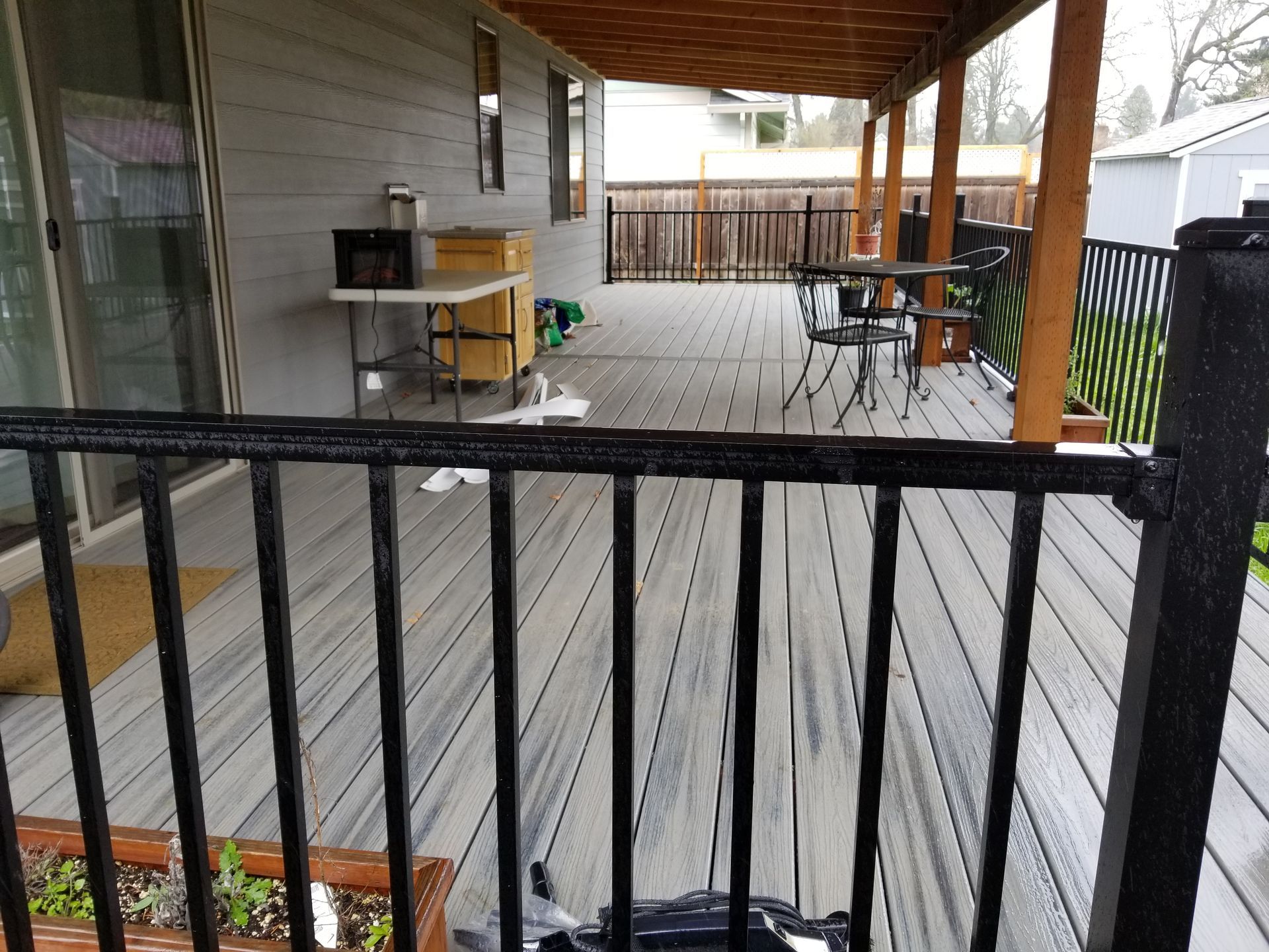 Covered wooden porch with black railing, gray deck boards, and outdoor grill near a table and chairs.