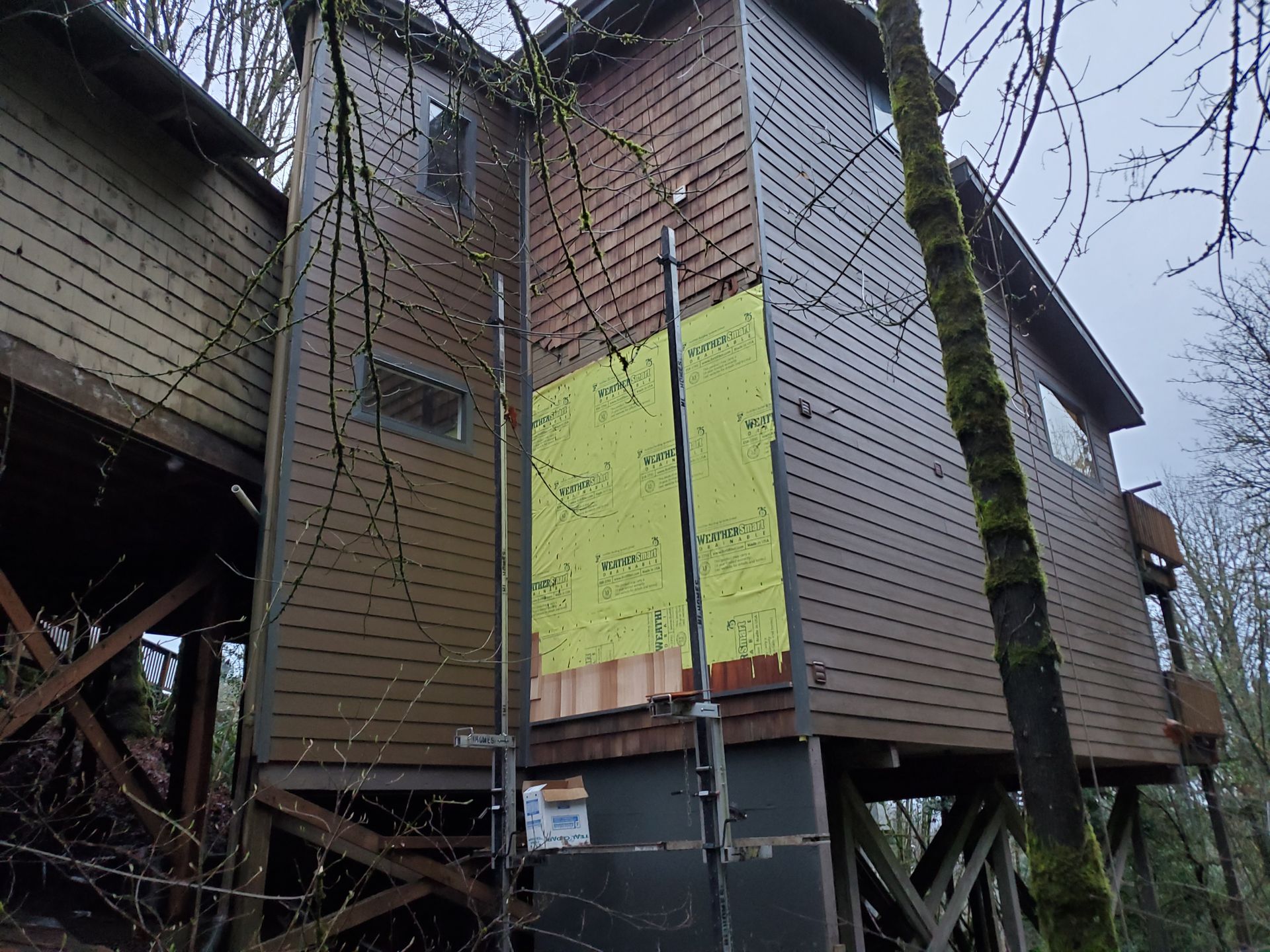 Stilted wooden house with green plywood boards on a wall under construction or repair