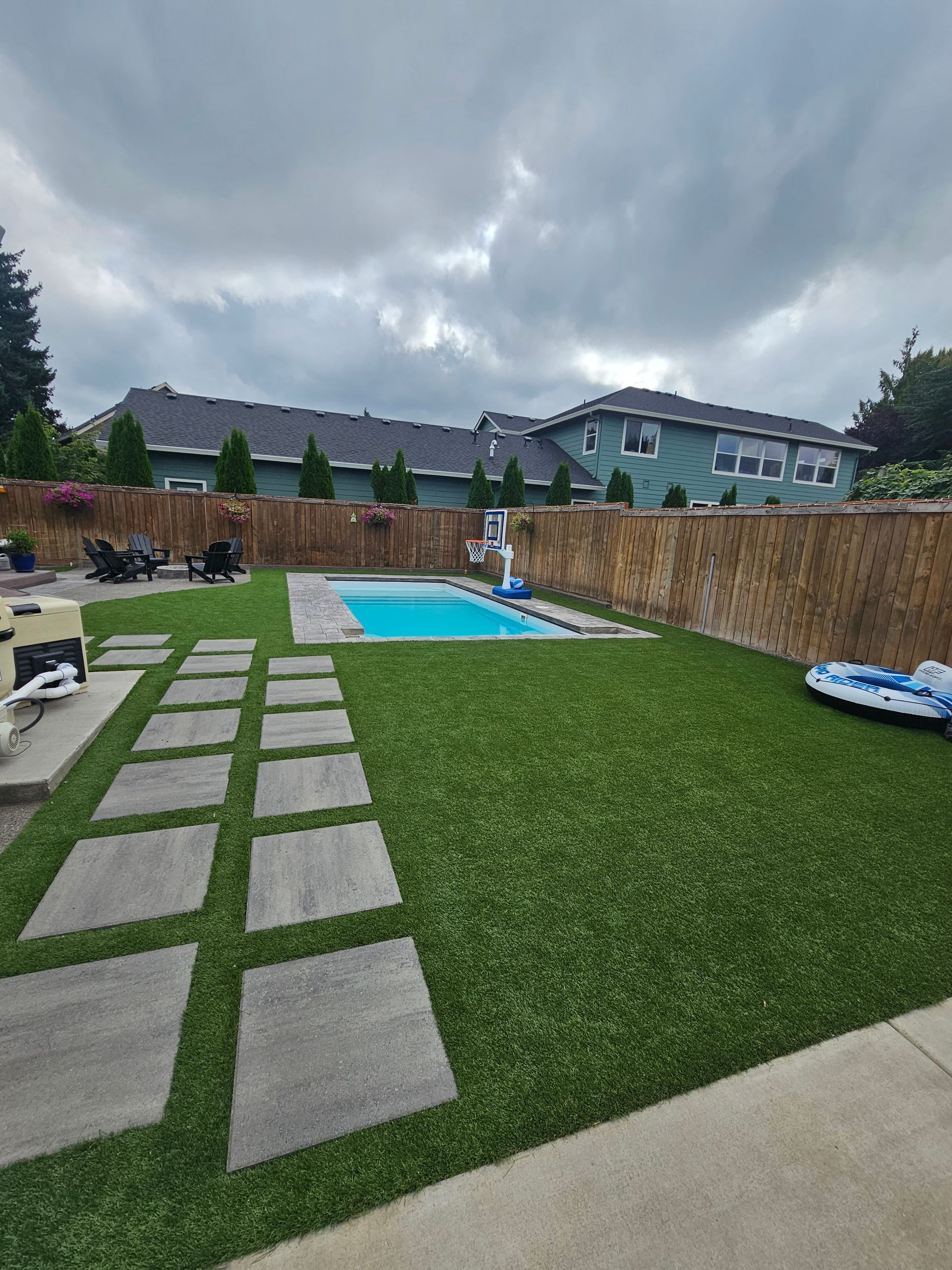 Backyard with stepping-stone path, green lawn, and a blue swimming pool under cloudy skies