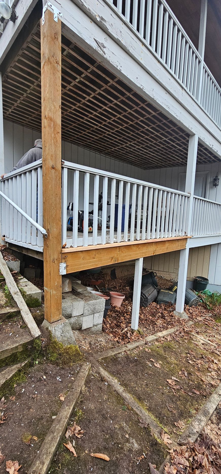 A weathered wooden staircase and porch with white railings beside a house, showing worn supports and ground below