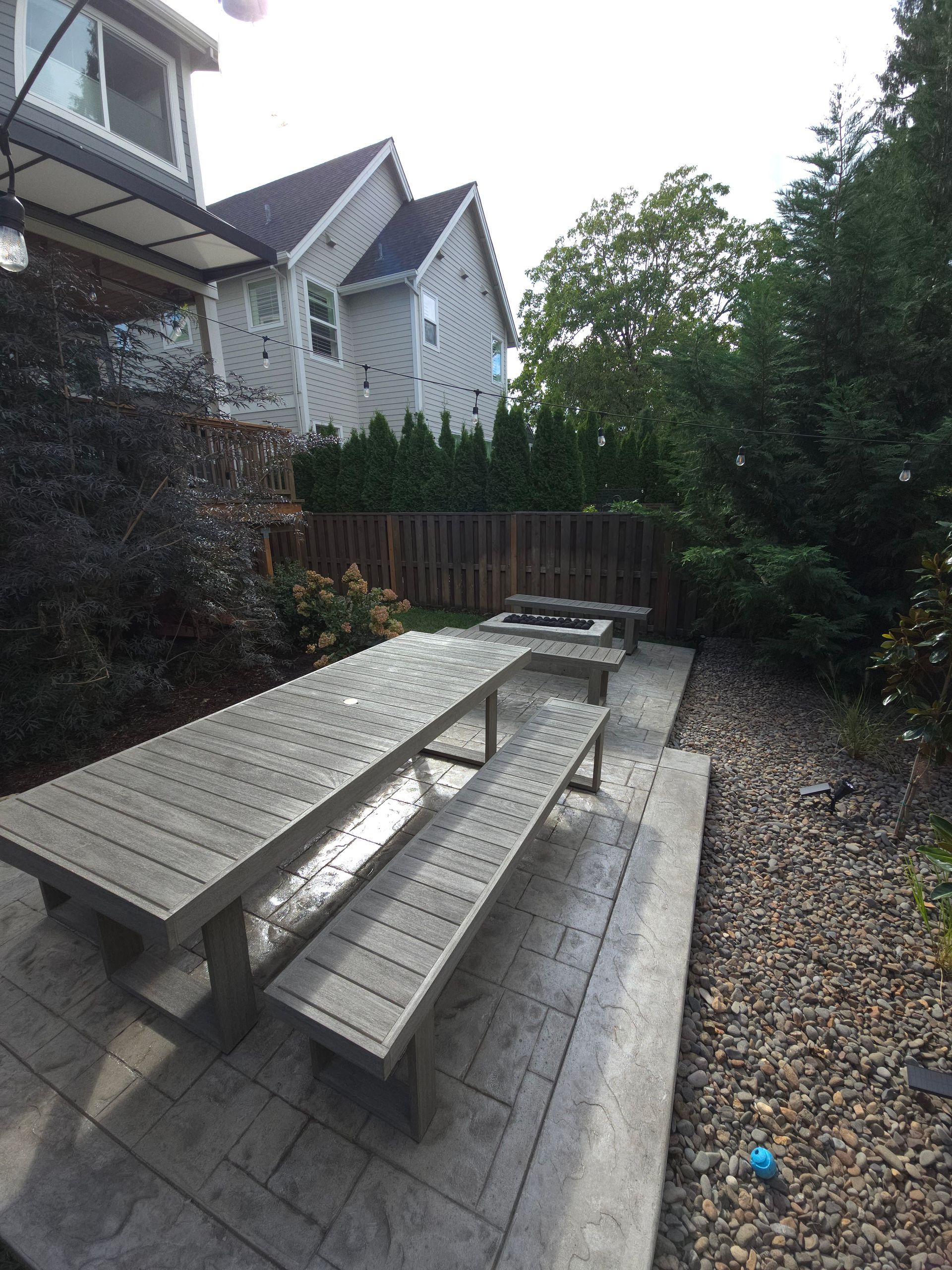 Backyard patio with wooden picnic table, paver stones, gravel, fence, and house siding
