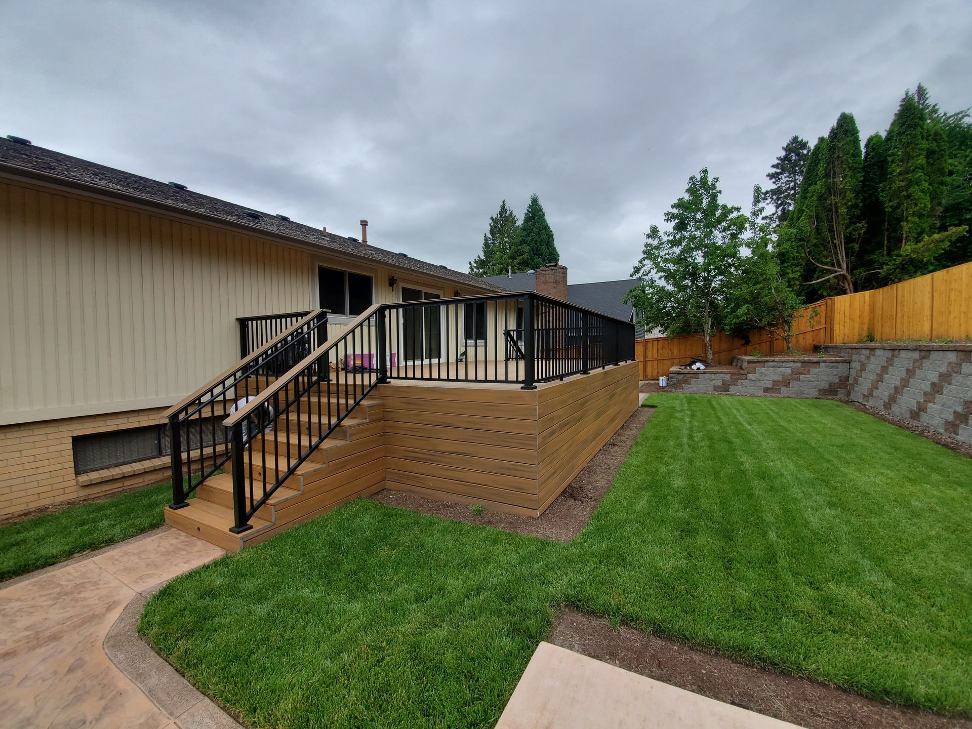 Backyard deck with stairs beside a beige house, overlooking a green lawn and wooden fence