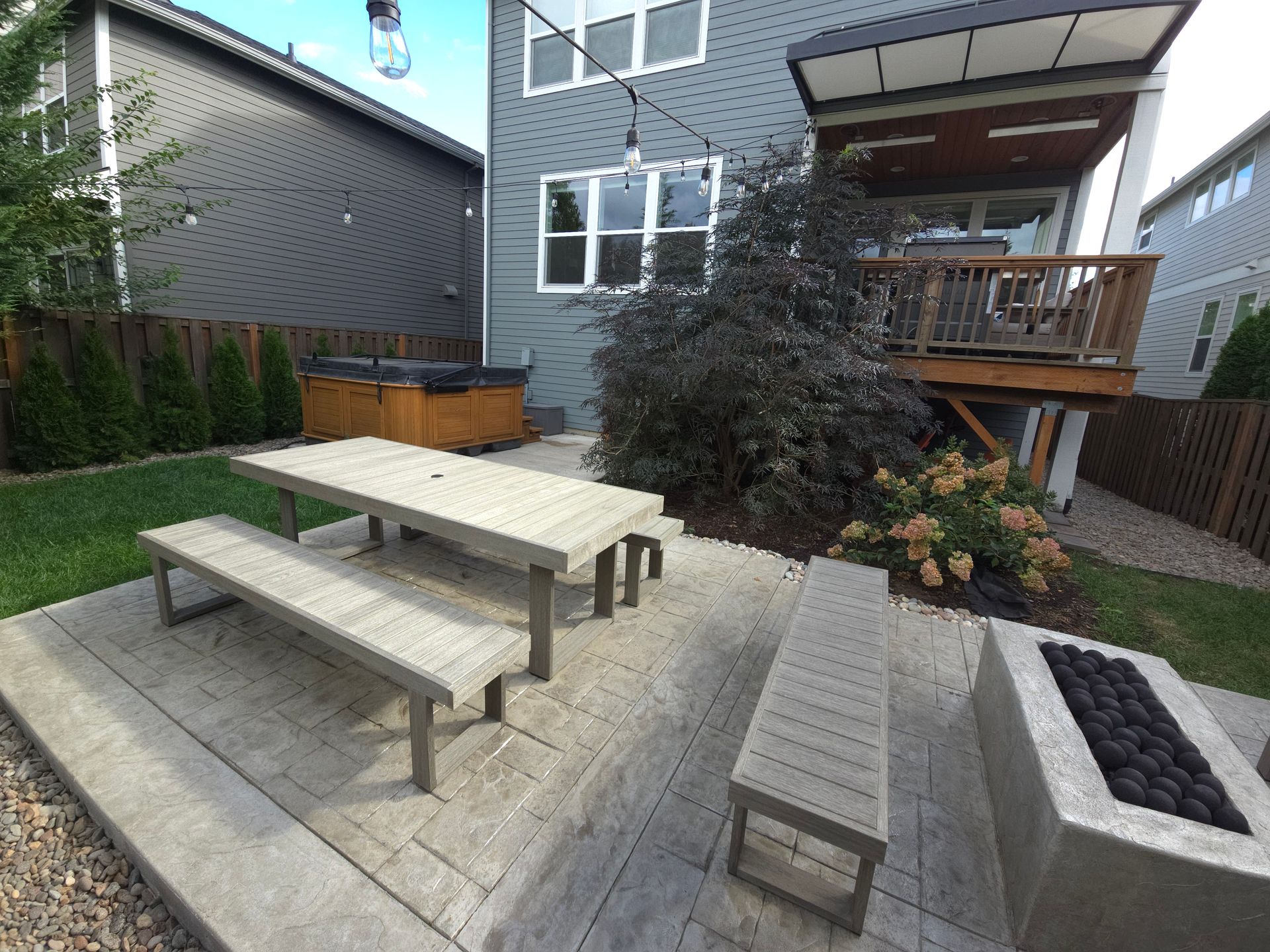 Backyard patio with picnic table, benches, raised fire pit, and modern house deck.
