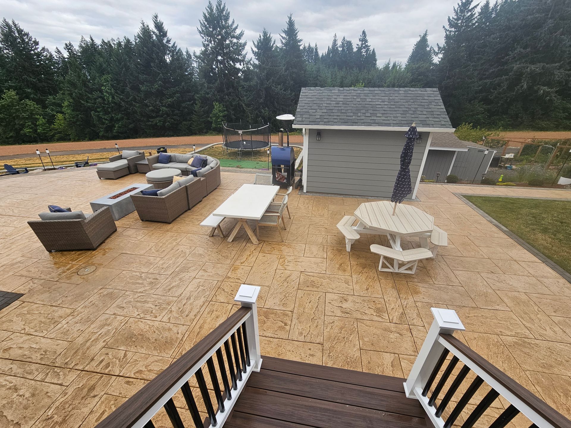 Backyard patio with outdoor seating, picnic tables, and a small shed, viewed from porch steps