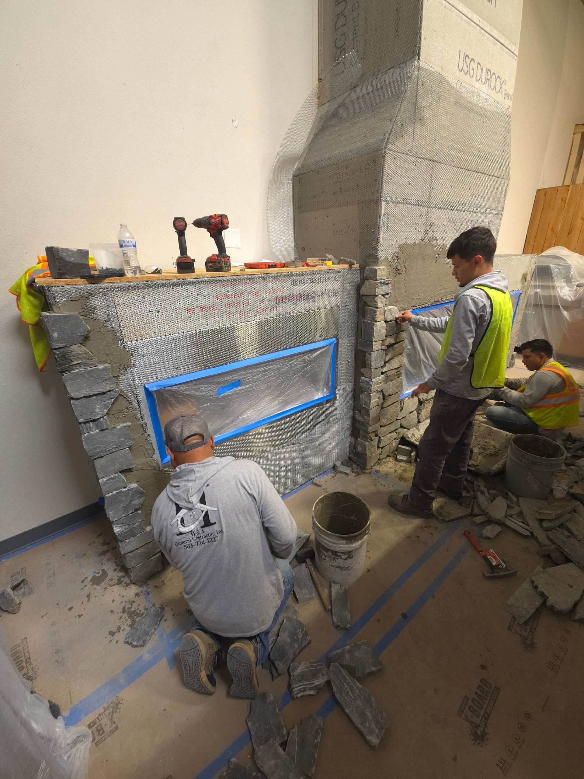 Workers installing a stone facade around a fireplace in a room under construction.