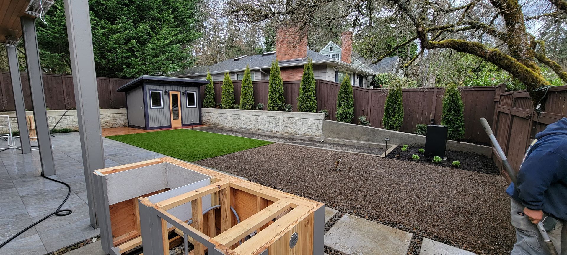 Backyard patio under construction with wooden framing, gravel path, and garden shed