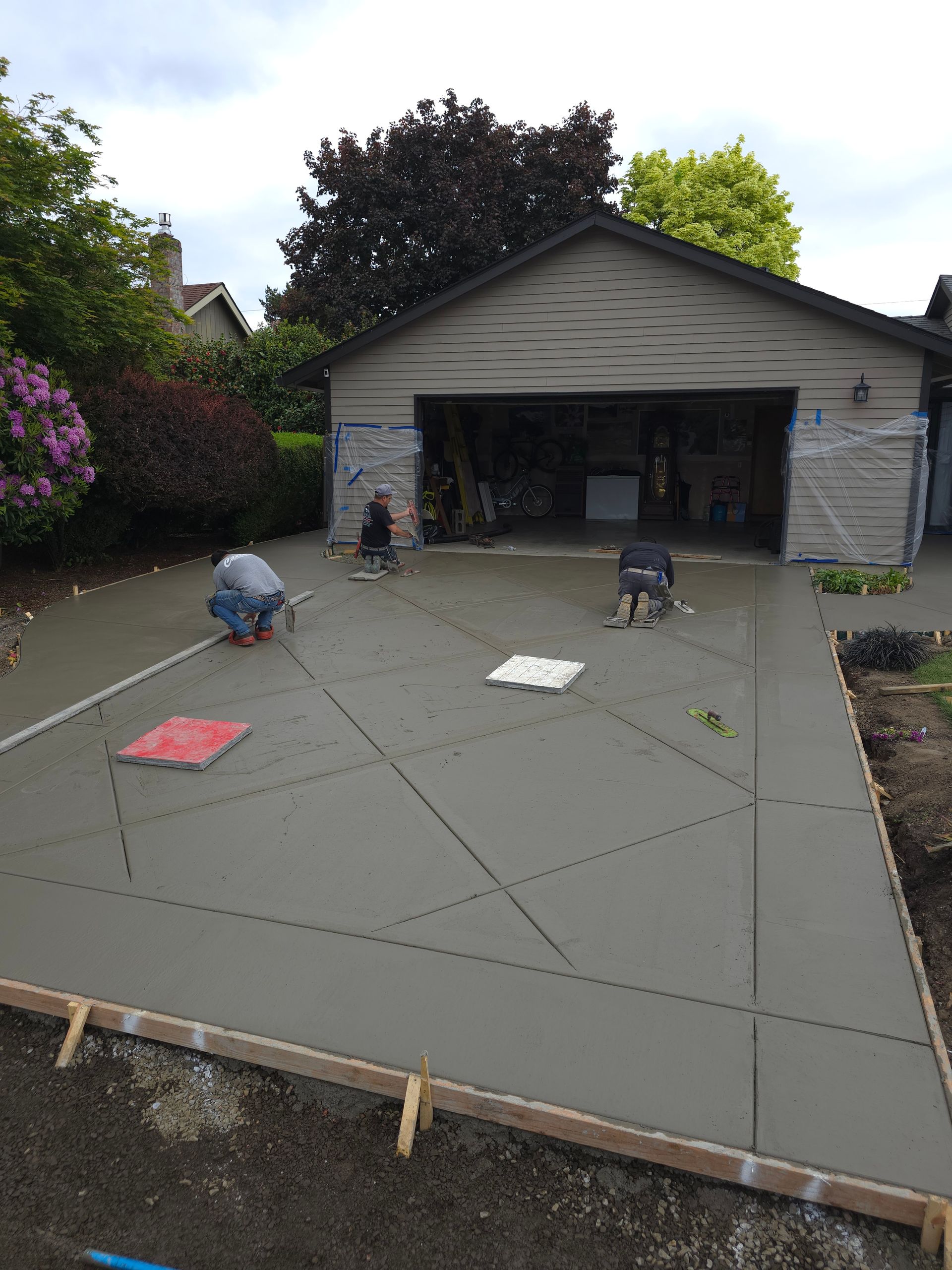 Workers pouring and smoothing concrete in a driveway beside a garage.