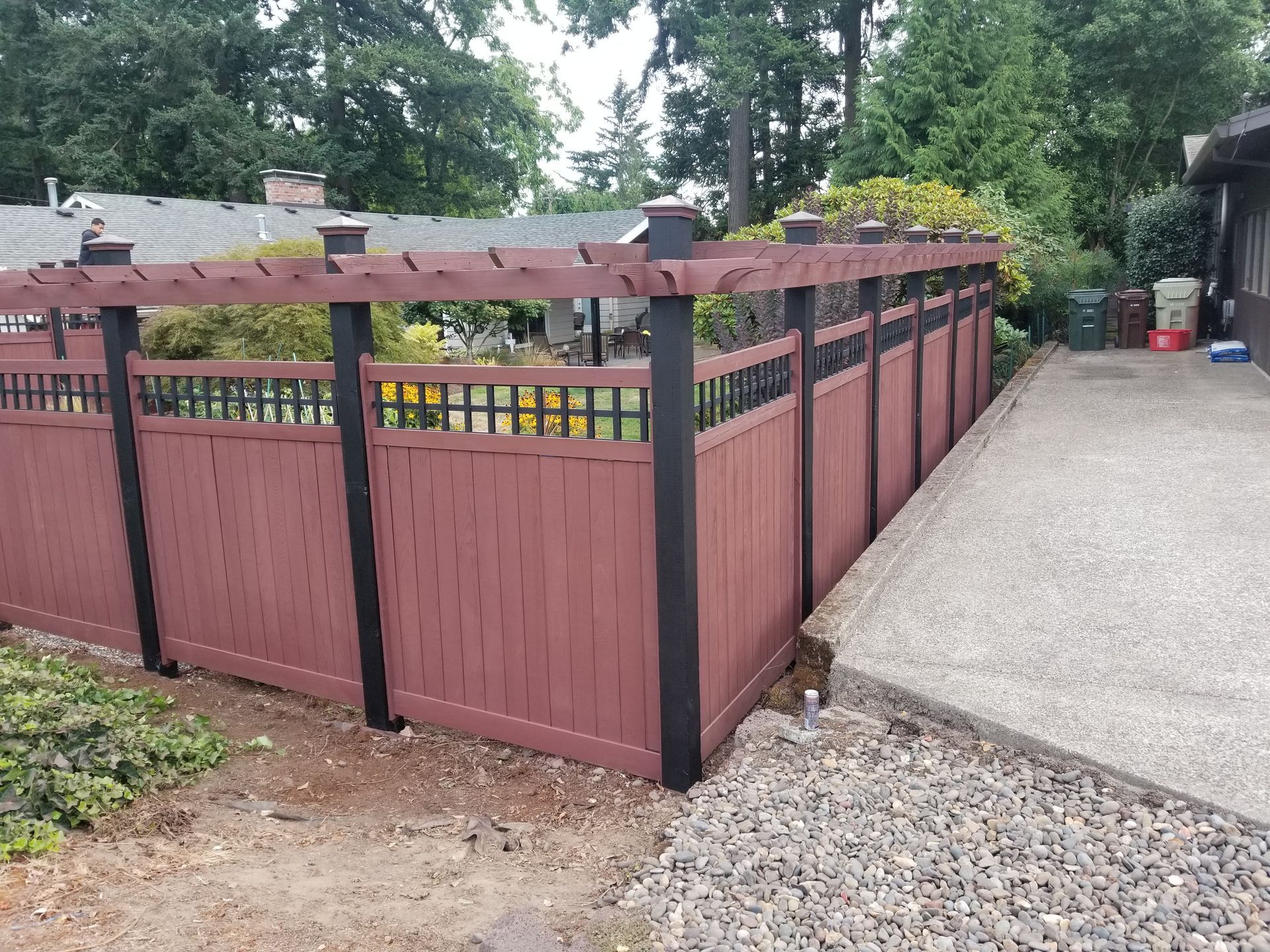 Maroon fenced deck beside a gravel driveway, with trees and a house in the background