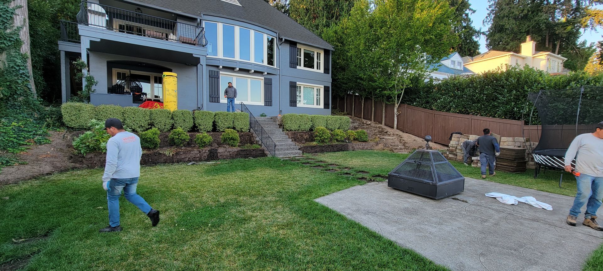People walking in a yard beside a modern house, with a patio and fire pit area in the foreground