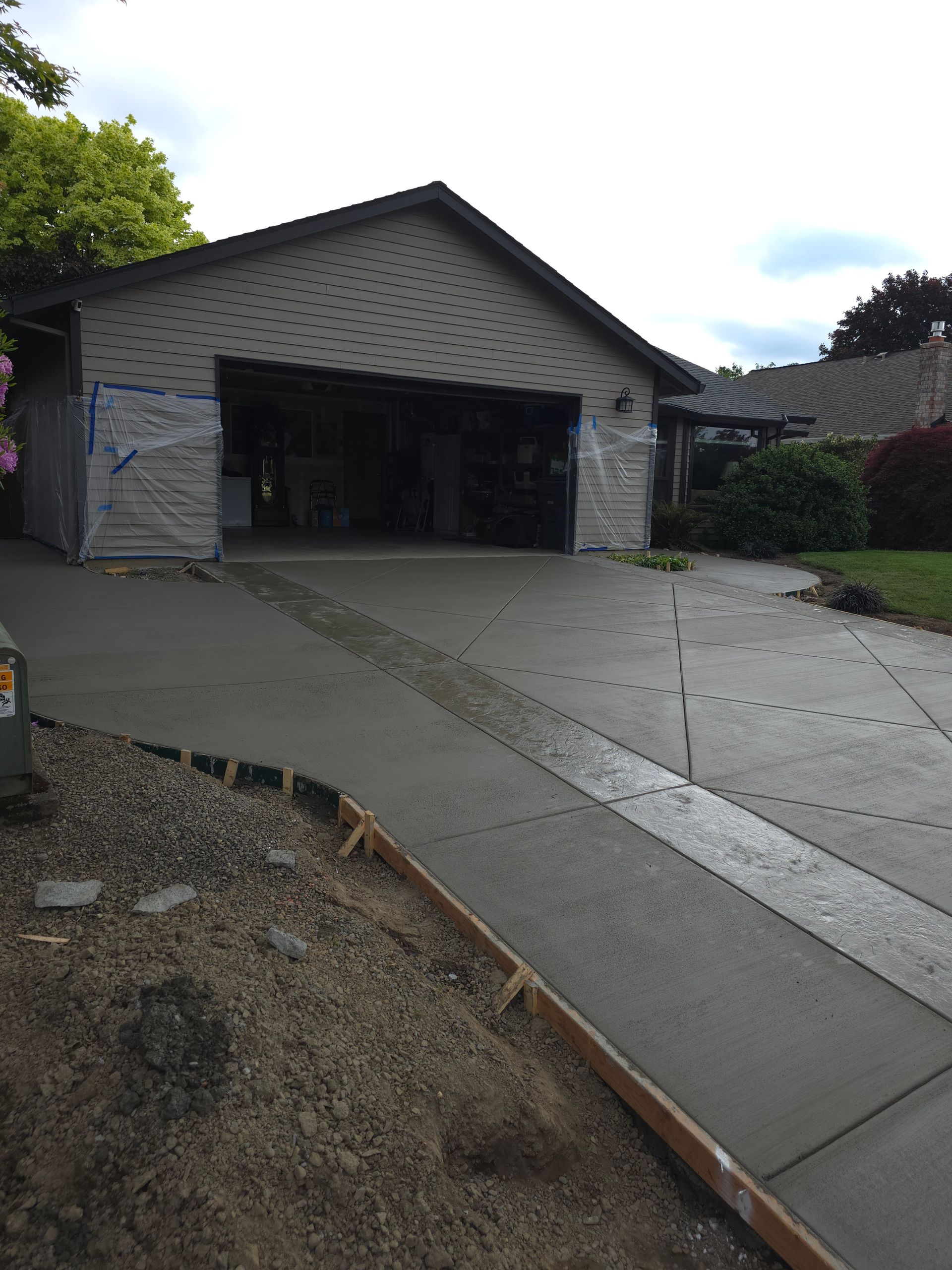Concrete driveway leading to an open two-car garage beside a house on a rainy day