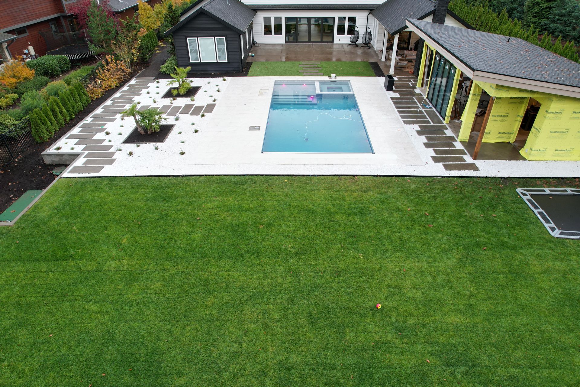 Backyard with a pool, white patio, lounge chairs, and a large green lawn