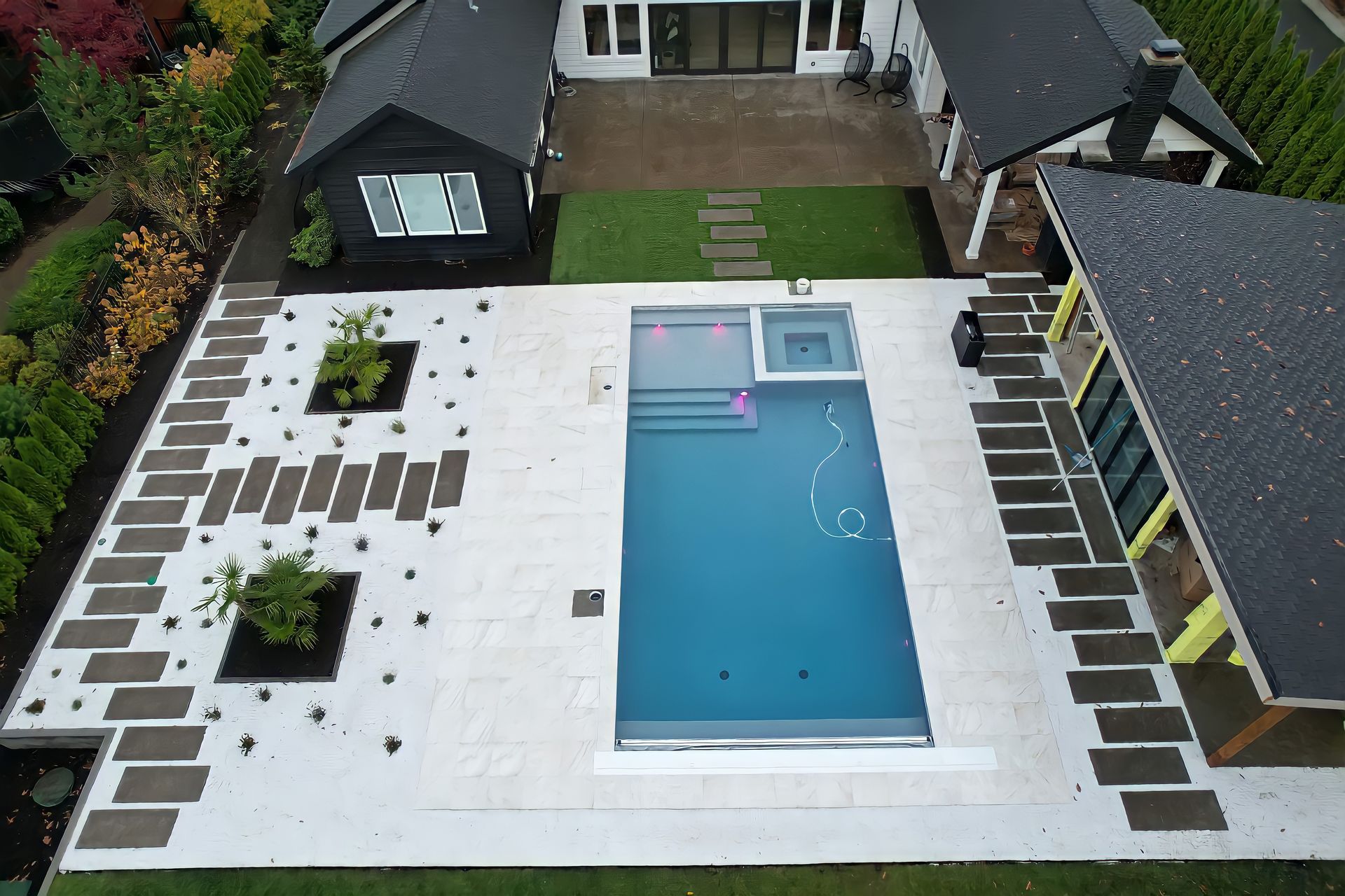 Aerial view of a backyard with a rectangular swimming pool, white patio, and lounge chairs.