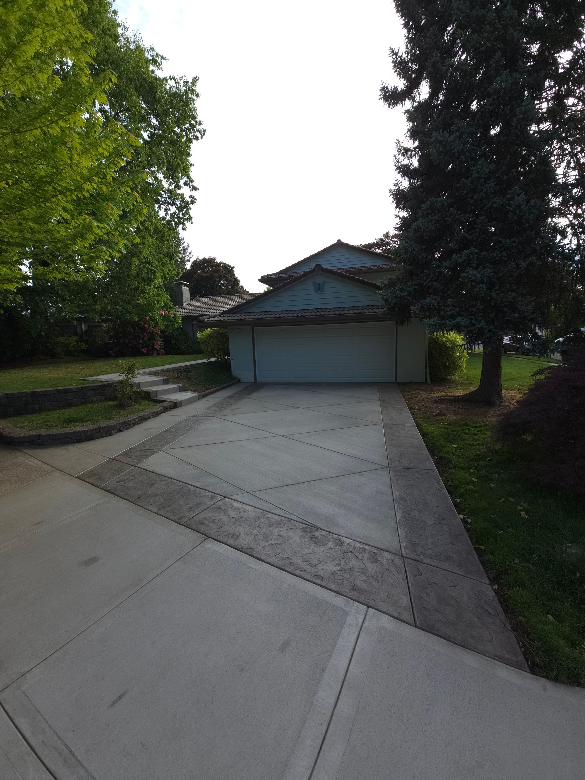 Suburban driveway leading to a garage with trees and a house in the background.
