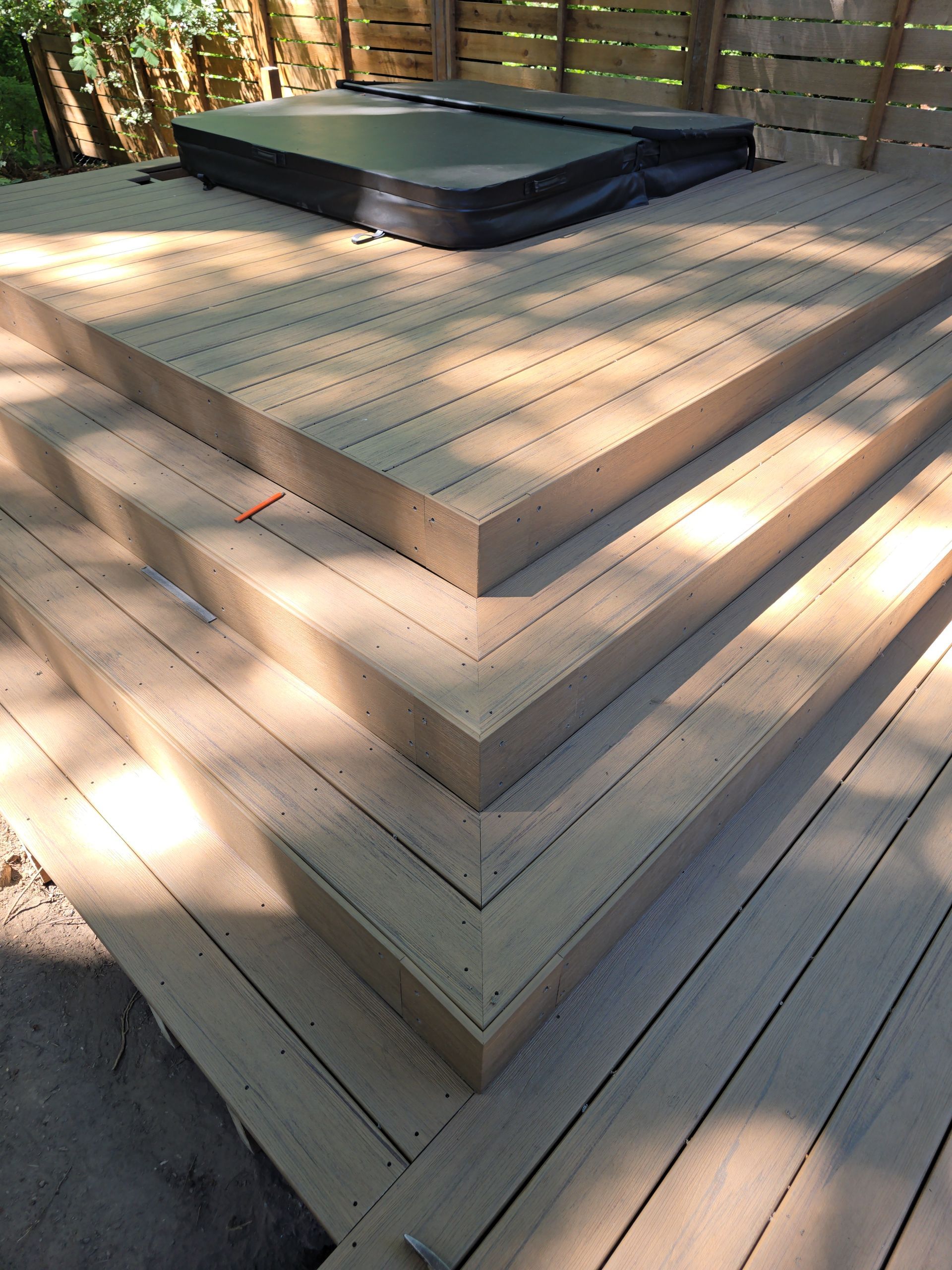 Wooden deck with tiered steps and a black rectangular platform on top, outdoors in sunlight