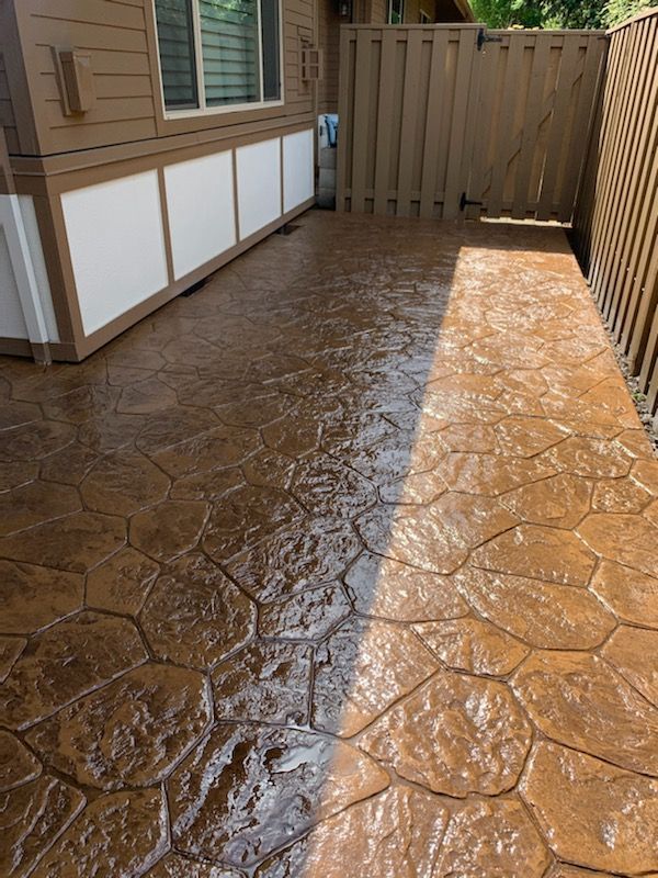 Stamped concrete patio beside a house and wooden fence, wet and sunlit.
