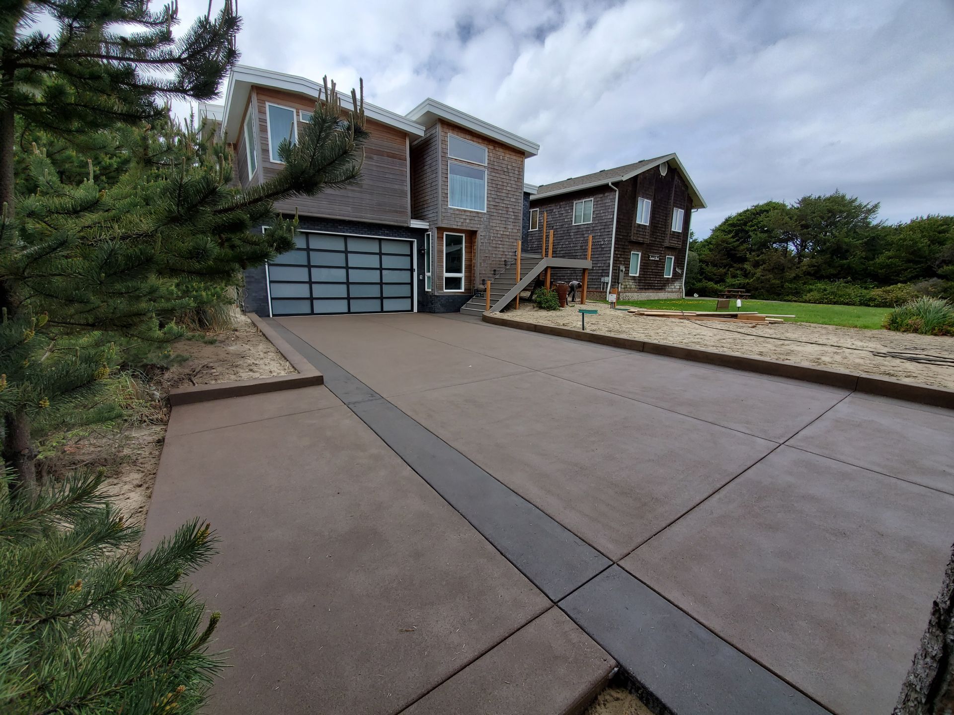 Modern stone house with a wide driveway, garage, and landscaped front yard under cloudy skies