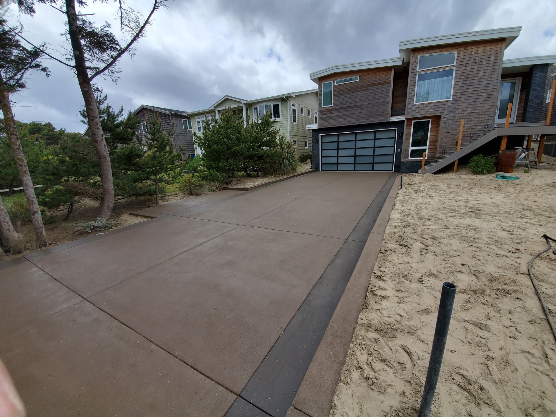 Concrete driveway leading to a modern house with a garage, under cloudy skies.