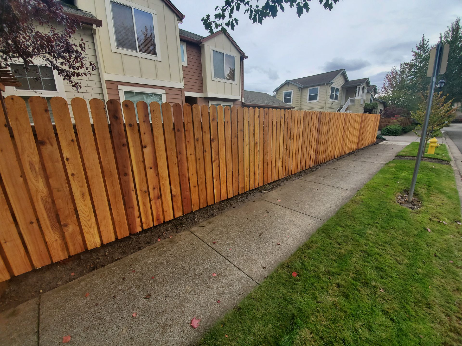 Residential sidewalk beside a long wooden fence and row houses on a cloudy day
