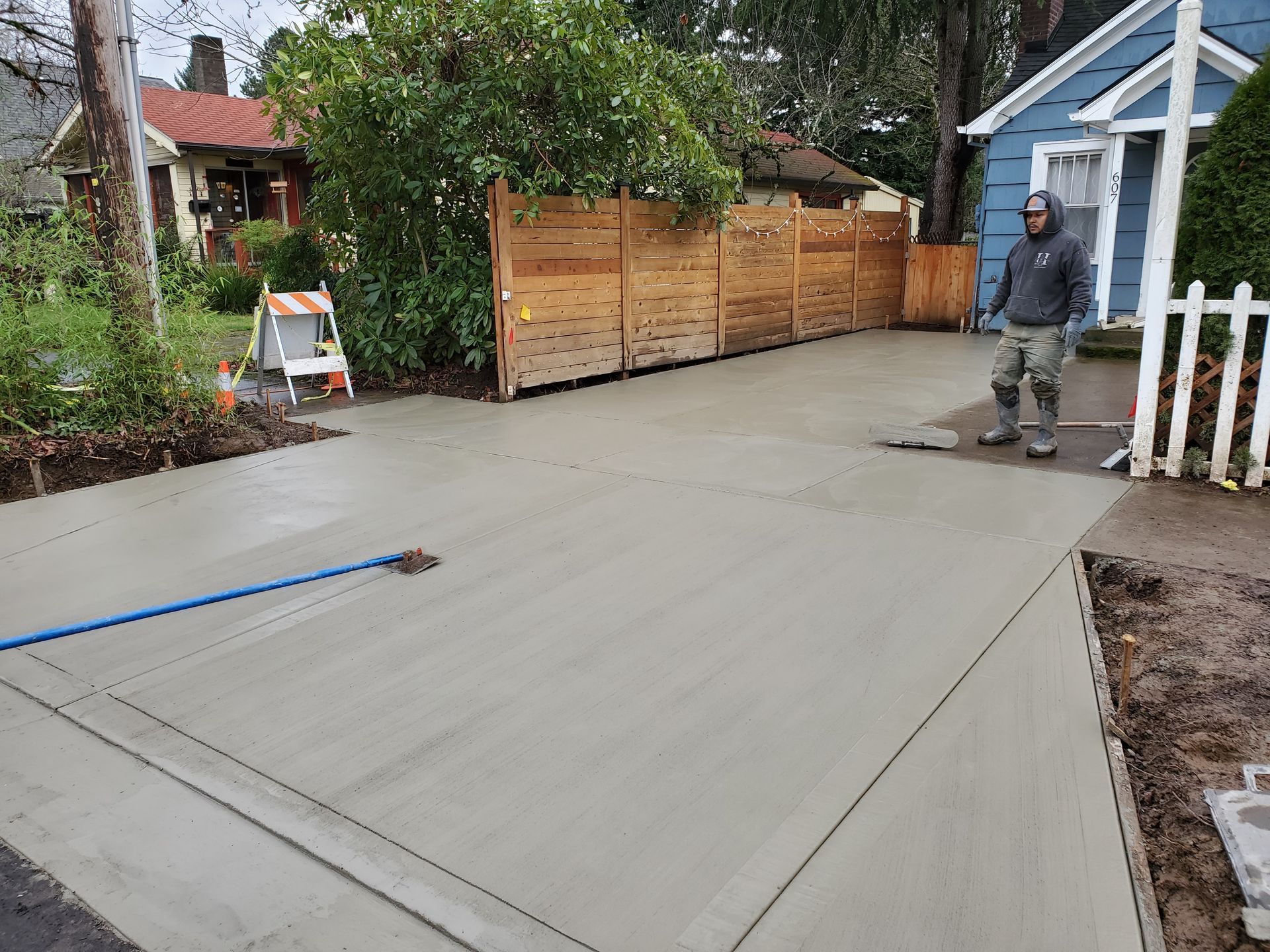 Freshly poured concrete driveway beside a house, with a worker standing near the edge.
