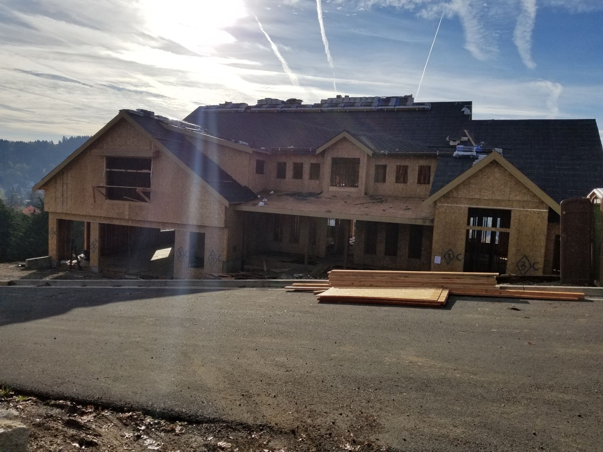 Large unfinished wooden house under construction on a sunny lot with mountains in the background