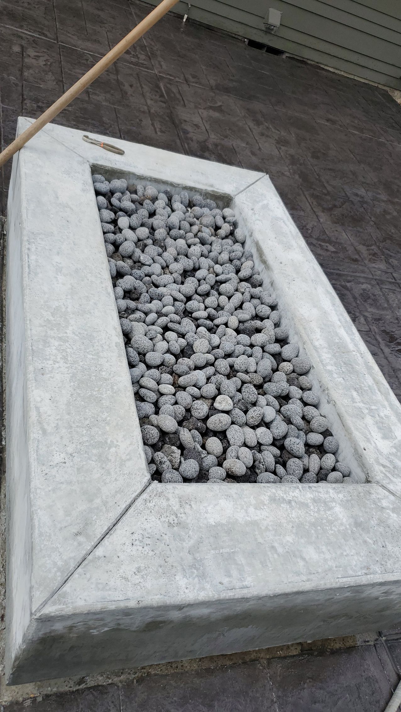 White rectangular planter filled with gray rocks on a concrete surface.