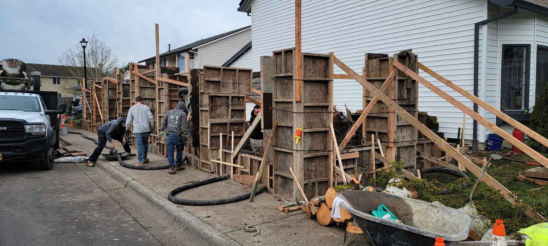 Workers setting up wooden concrete forms beside a house on a muddy construction site