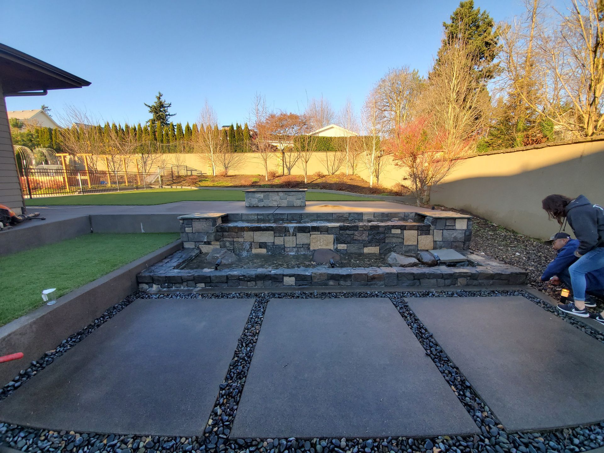 Backyard patio under construction with stone retaining wall and worker kneeling at right
