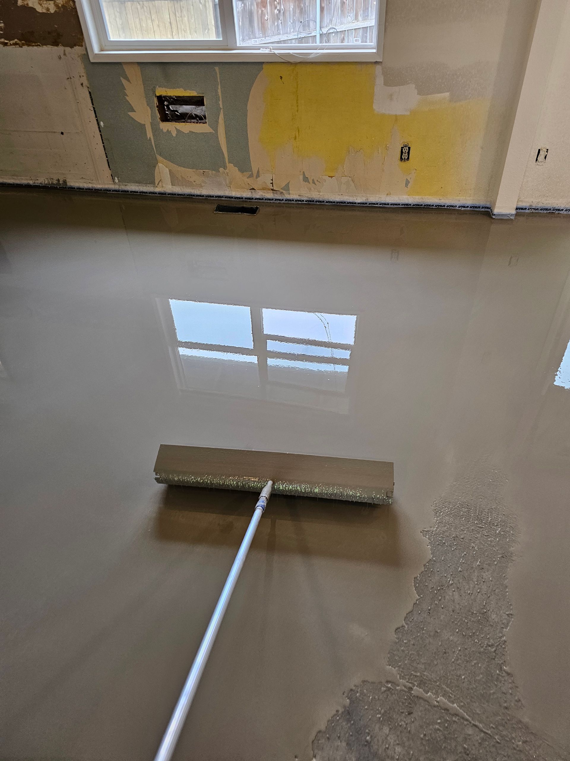 Wet floor being squeegeed indoors, with reflections of a window and peeling wall paint.