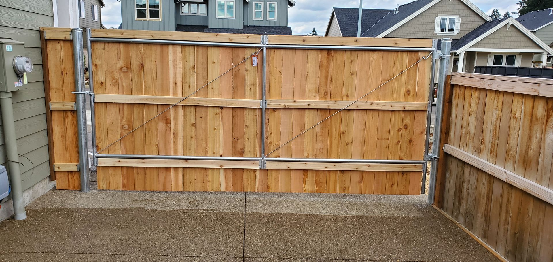 Wooden backyard fence enclosing a gravel area, with neighboring houses visible above it