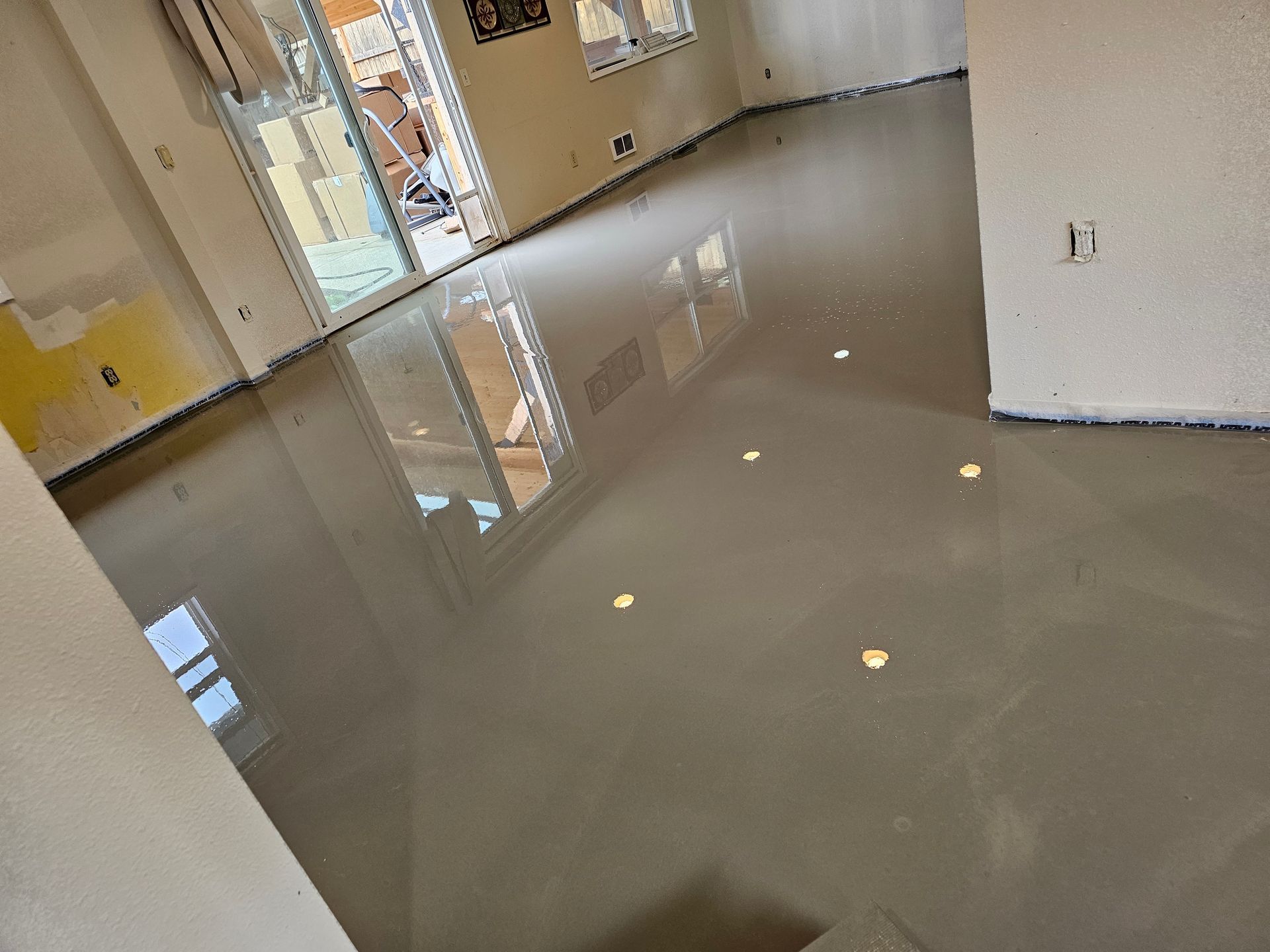 Glossy gray epoxy floor in an empty room with white walls and windows reflected on the surface