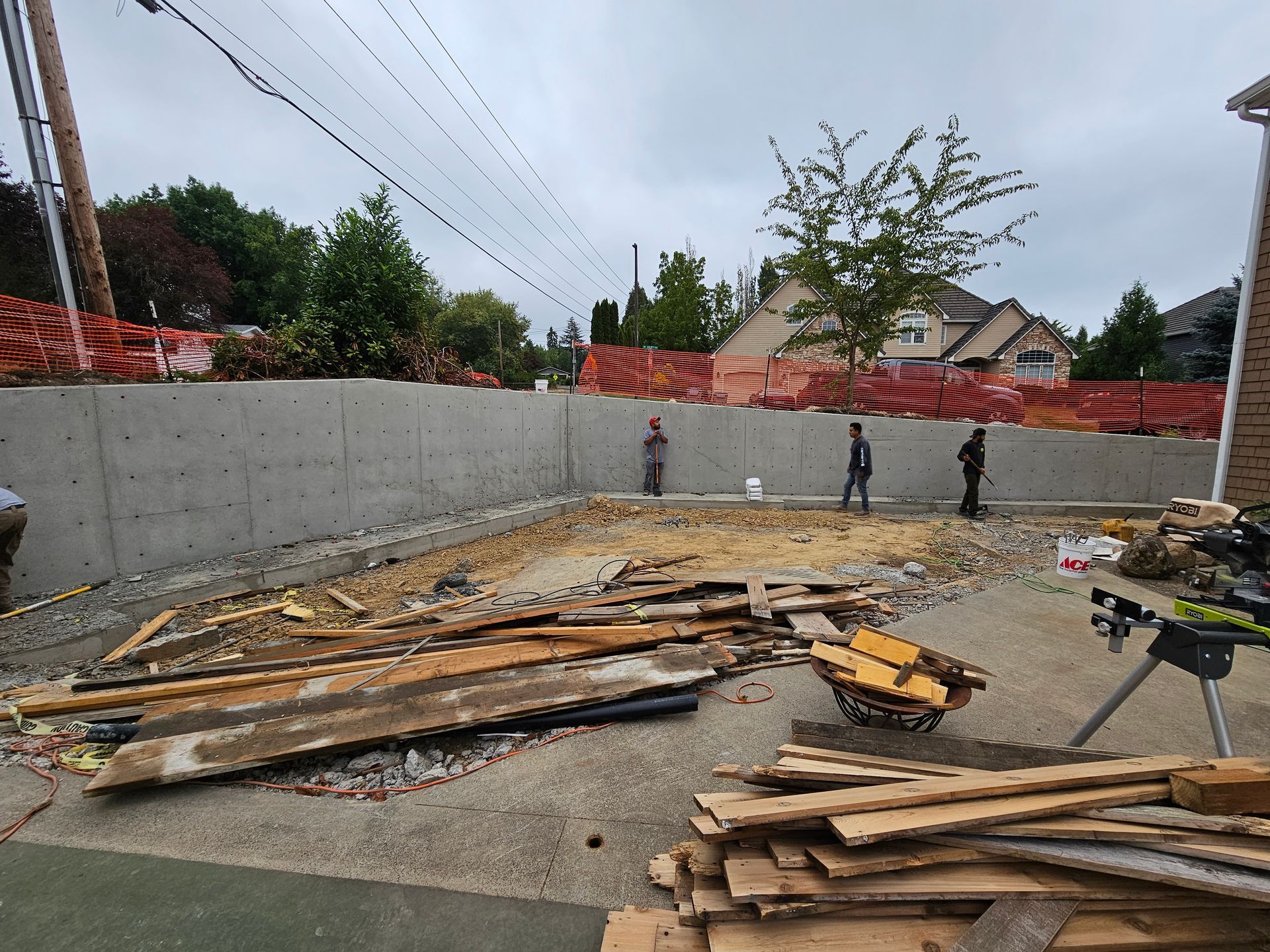 Construction site with concrete walls, scattered lumber, and workers along the back wall.