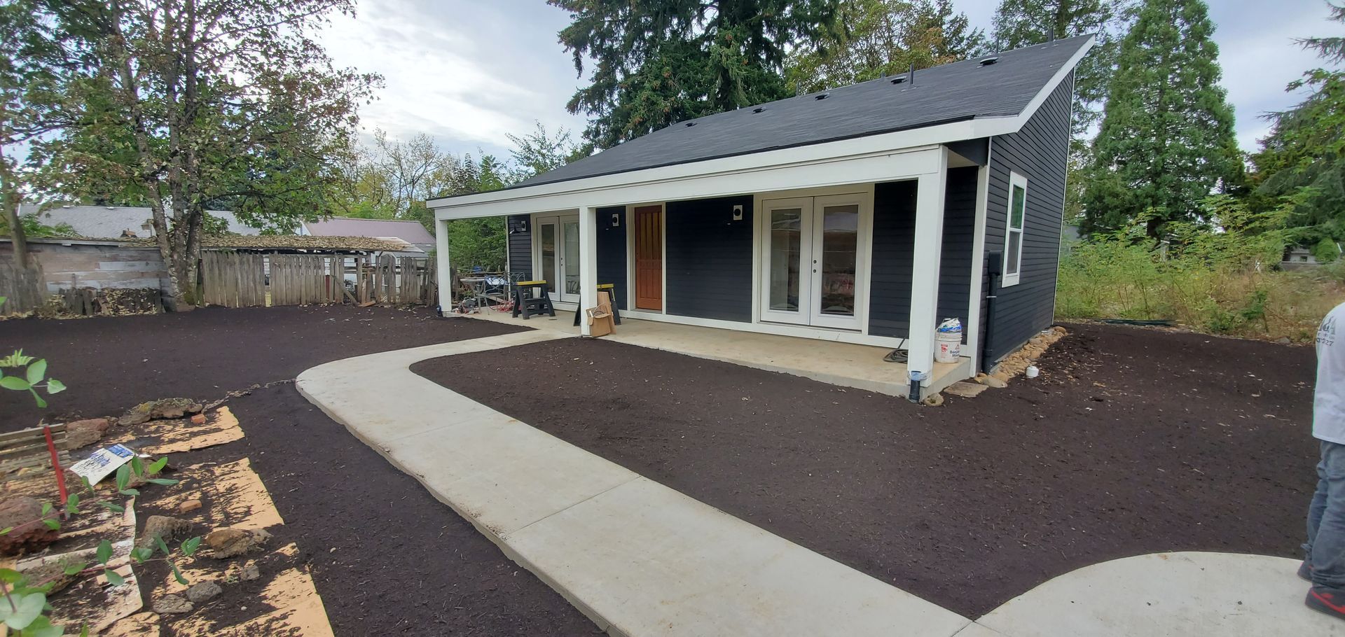 Modern single-story house with a covered porch, dark siding, and a curved concrete walkway in a landscaped yard