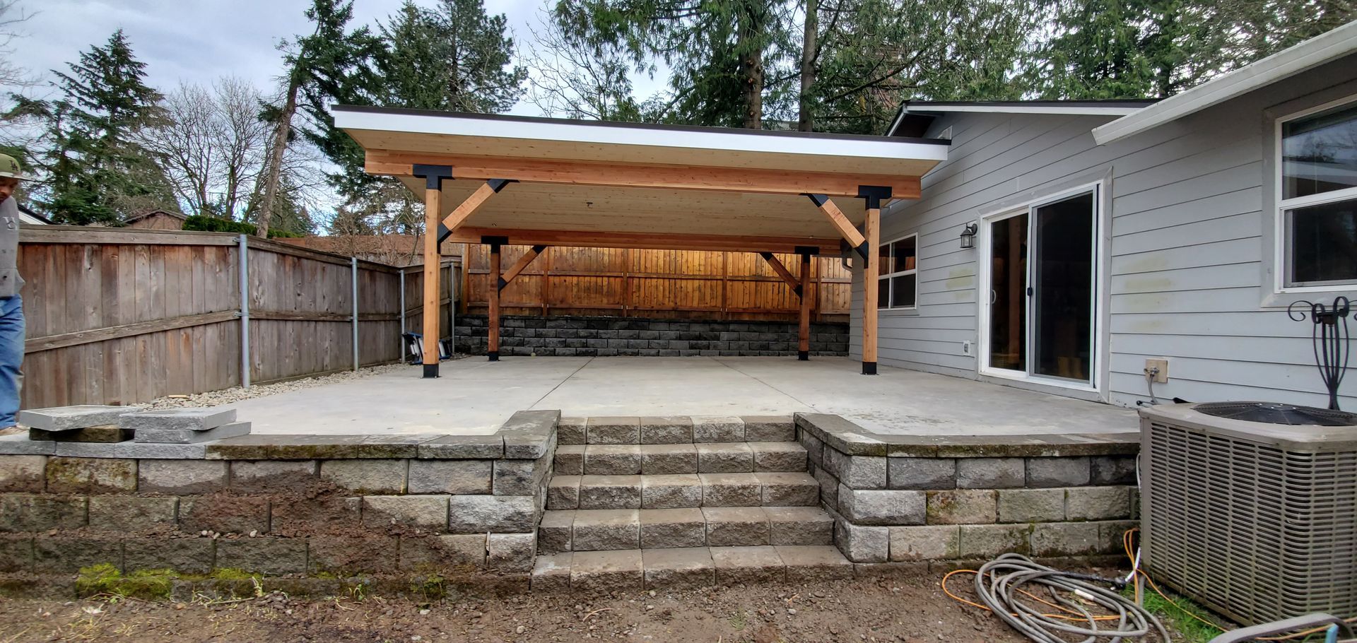Backyard patio with stone steps, raised deck, and wooden pergola beside a house