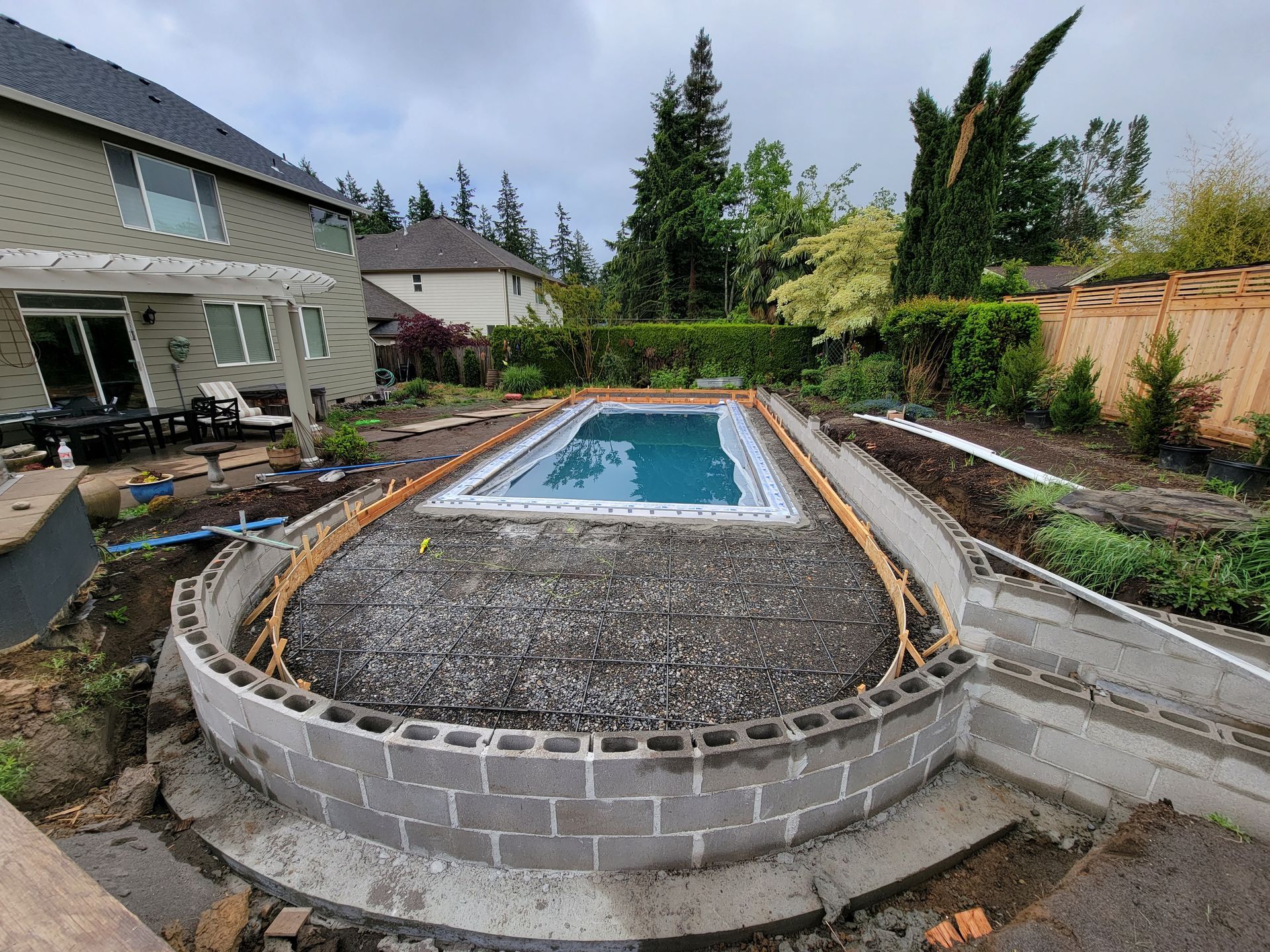 Backyard with a rectangular in-ground pool under construction, surrounded by gravel and concrete walls