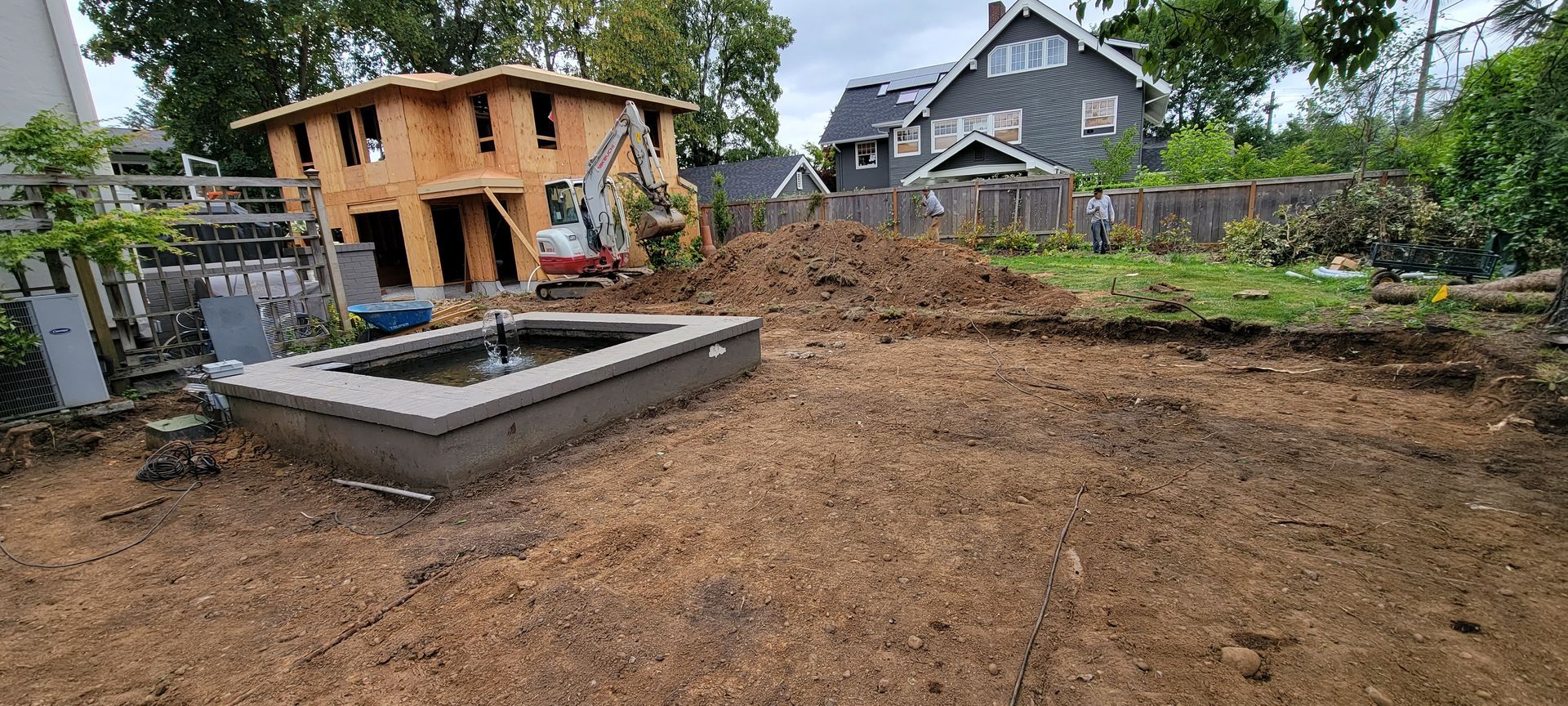 Backyard under construction with dirt ground, concrete footings, and a small wooden shed in the background