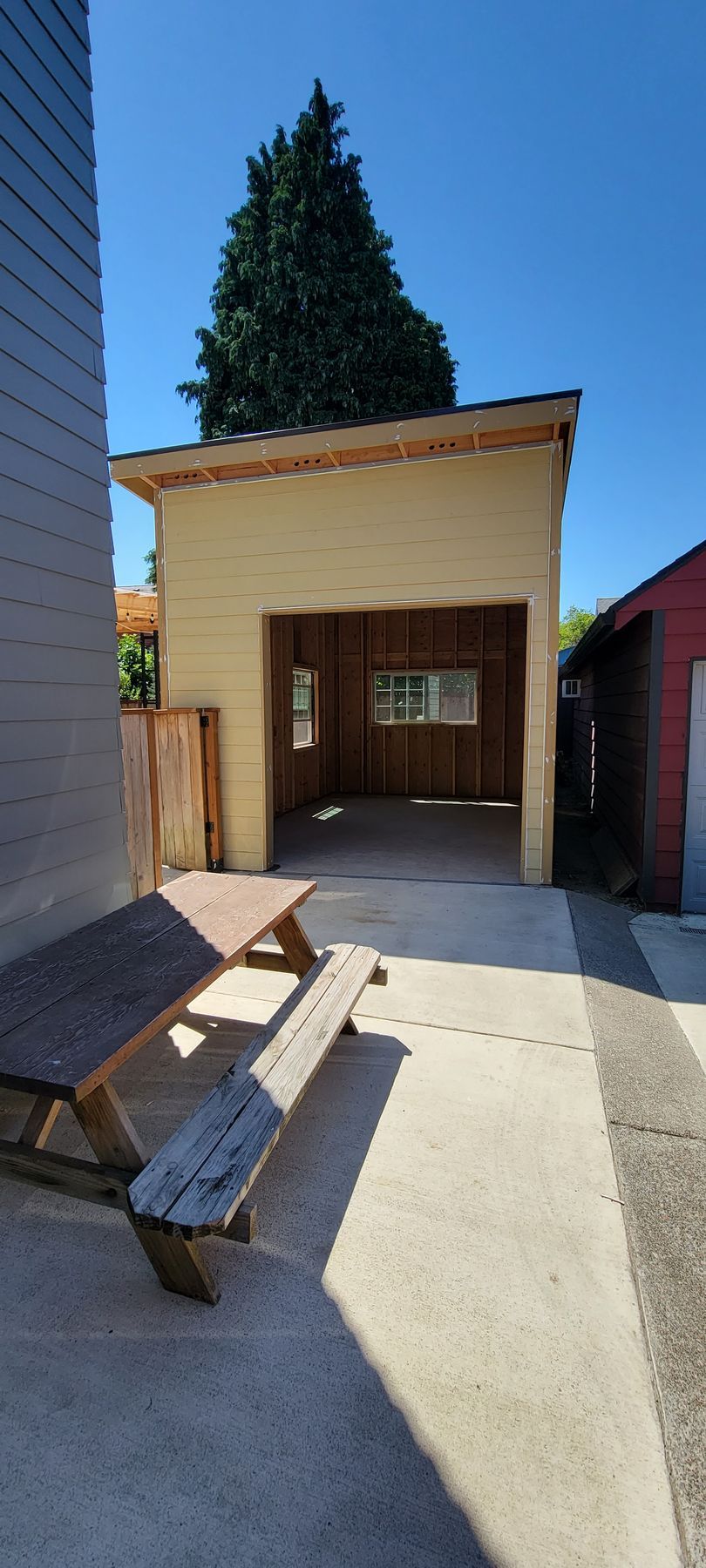 Small outdoor patio with a wooden bench, a covered entryway, and a tall tree behind it.