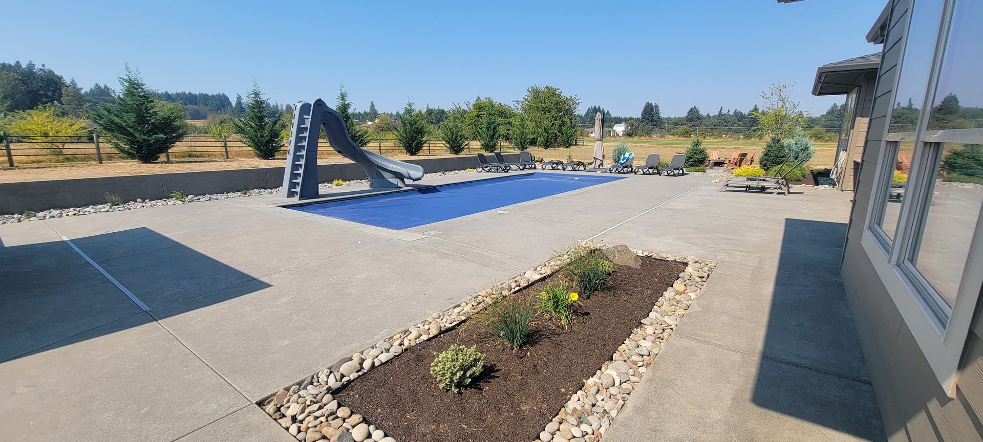 Outdoor playground with blue climbing structure, planter bed, and building wall under a sunny sky