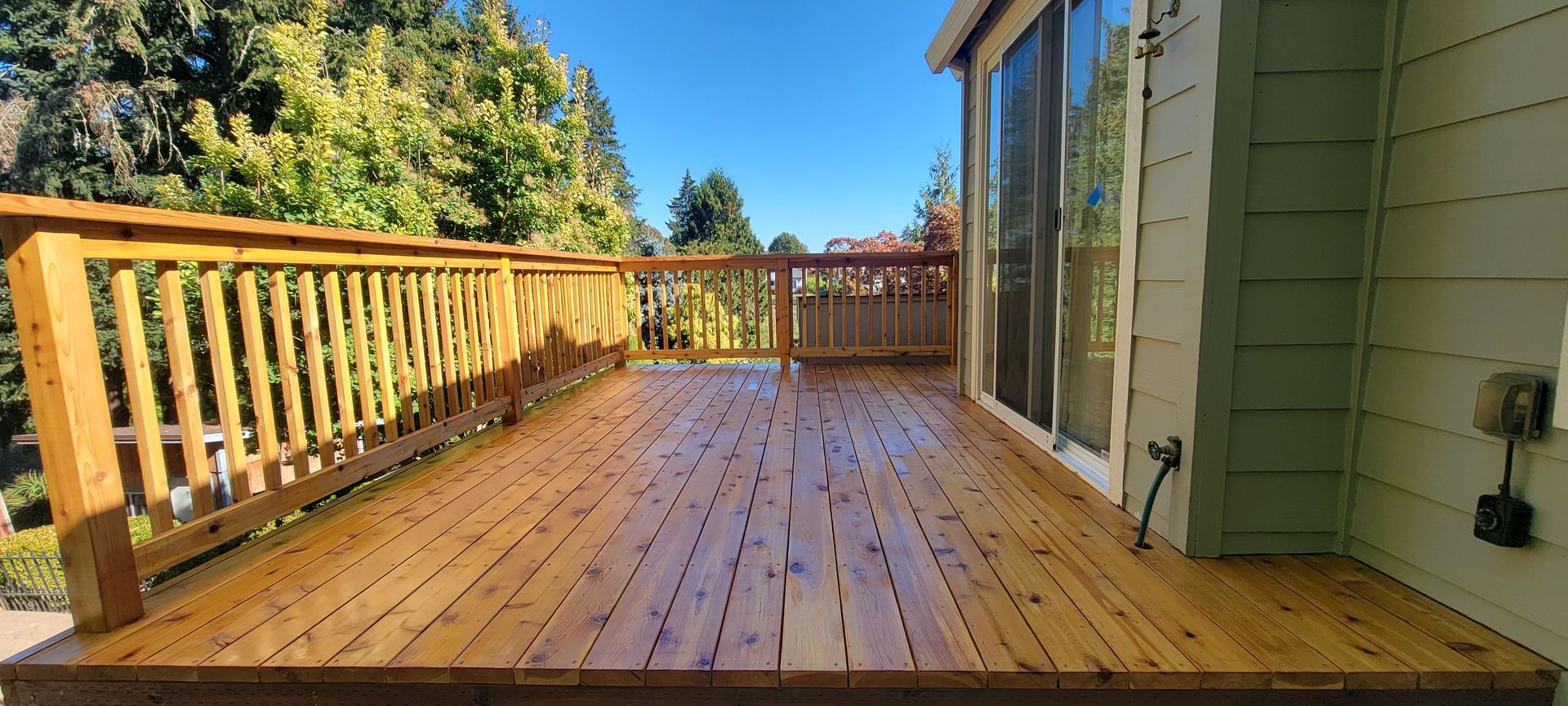 Wooden backyard deck with railing beside a house, in warm sunlight.