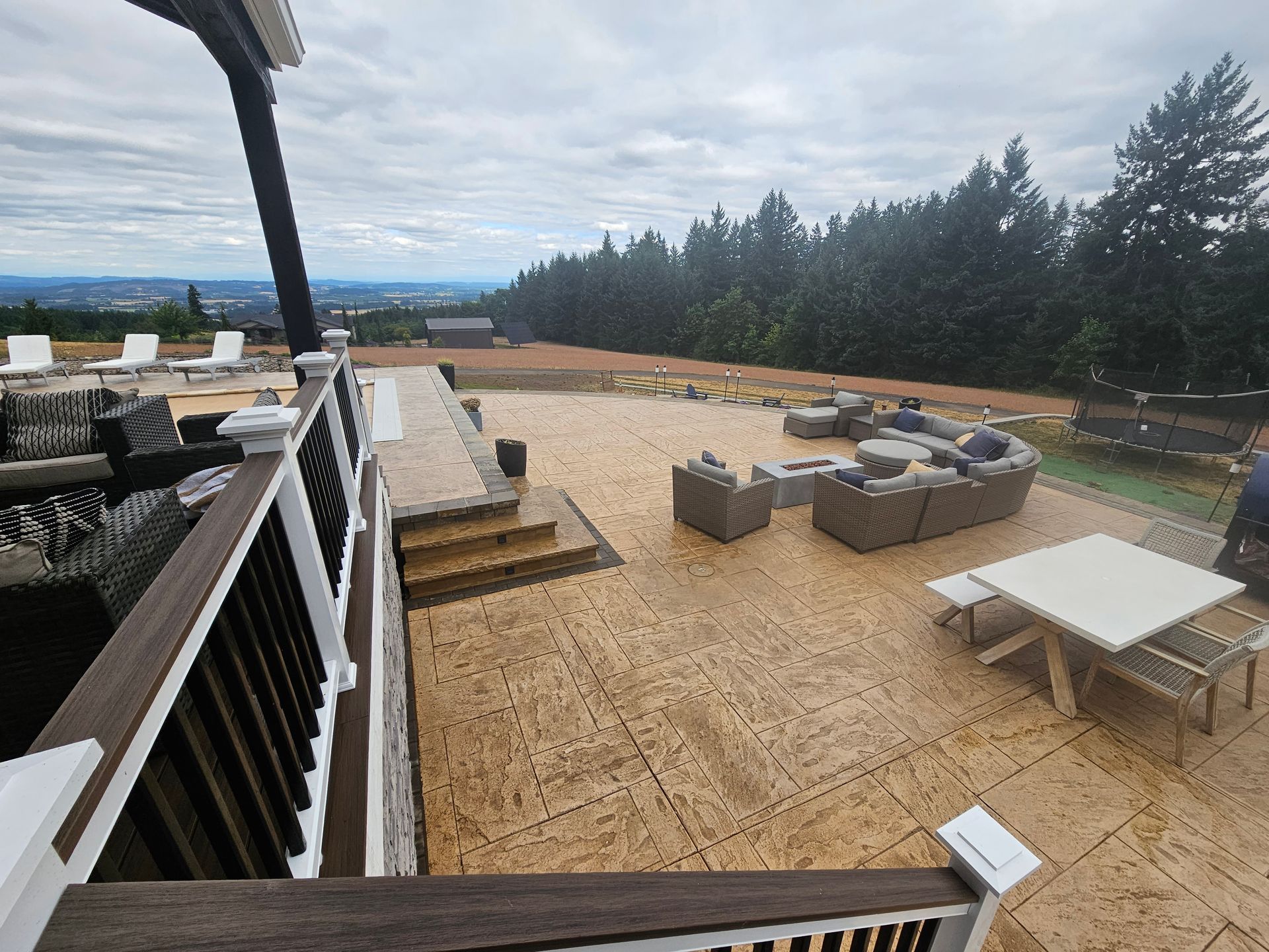 Patio with wicker seating and tables on a gravel terrace overlooking trees and a distant landscape