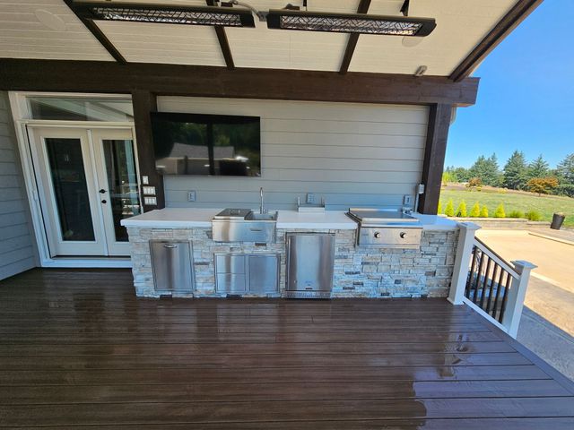 Covered wooden deck with outdoor kitchen, grill, sink, and white sliding doors overlooking open yard