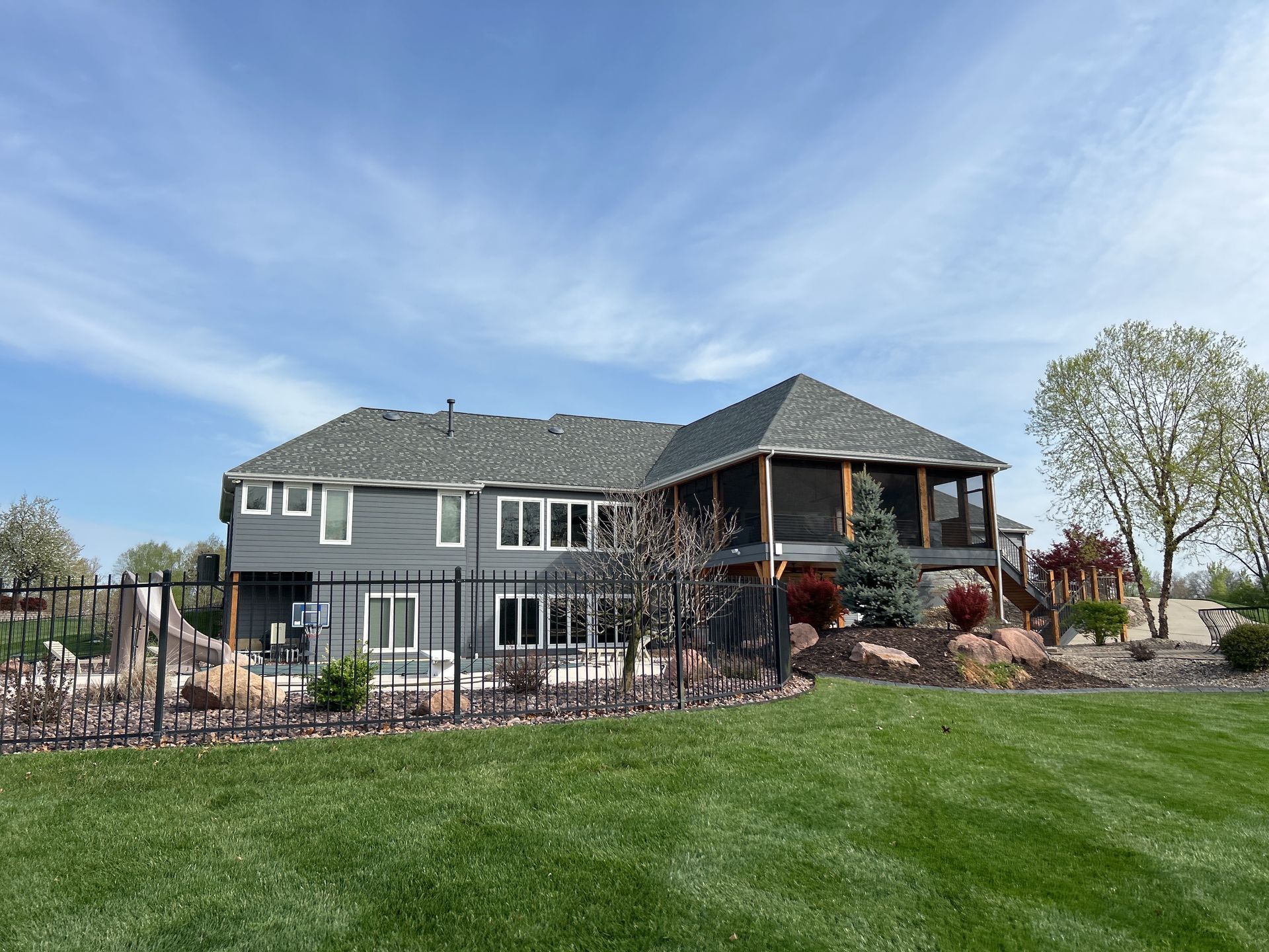 Gray house with a covered porch, landscaped yard, and green lawn under a blue sky