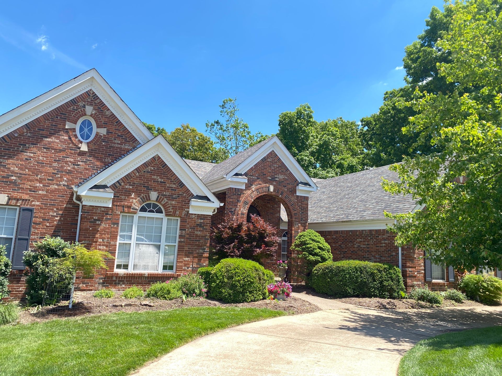 Brick suburban house with white trim, arched entry, and a curved driveway under a blue sky