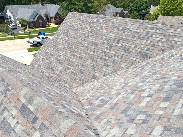 Close-up of a gray shingle roof with suburban houses in the background.
