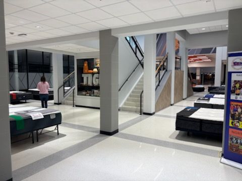 Bright mall food court with tables, stairs, kiosks, and a person walking in the background
